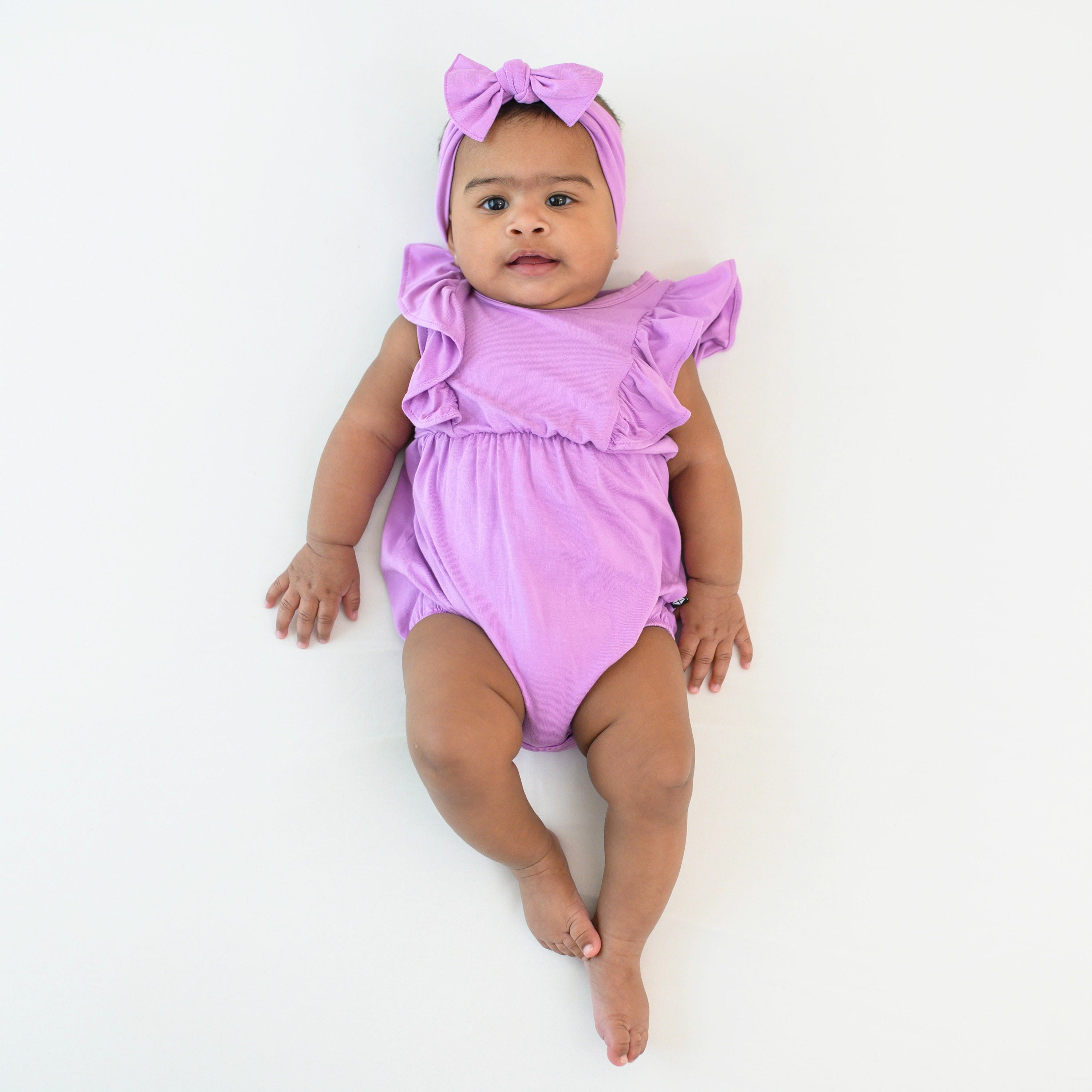 Infant wearing purple bubble romper in Poi with matching knotted bow headband