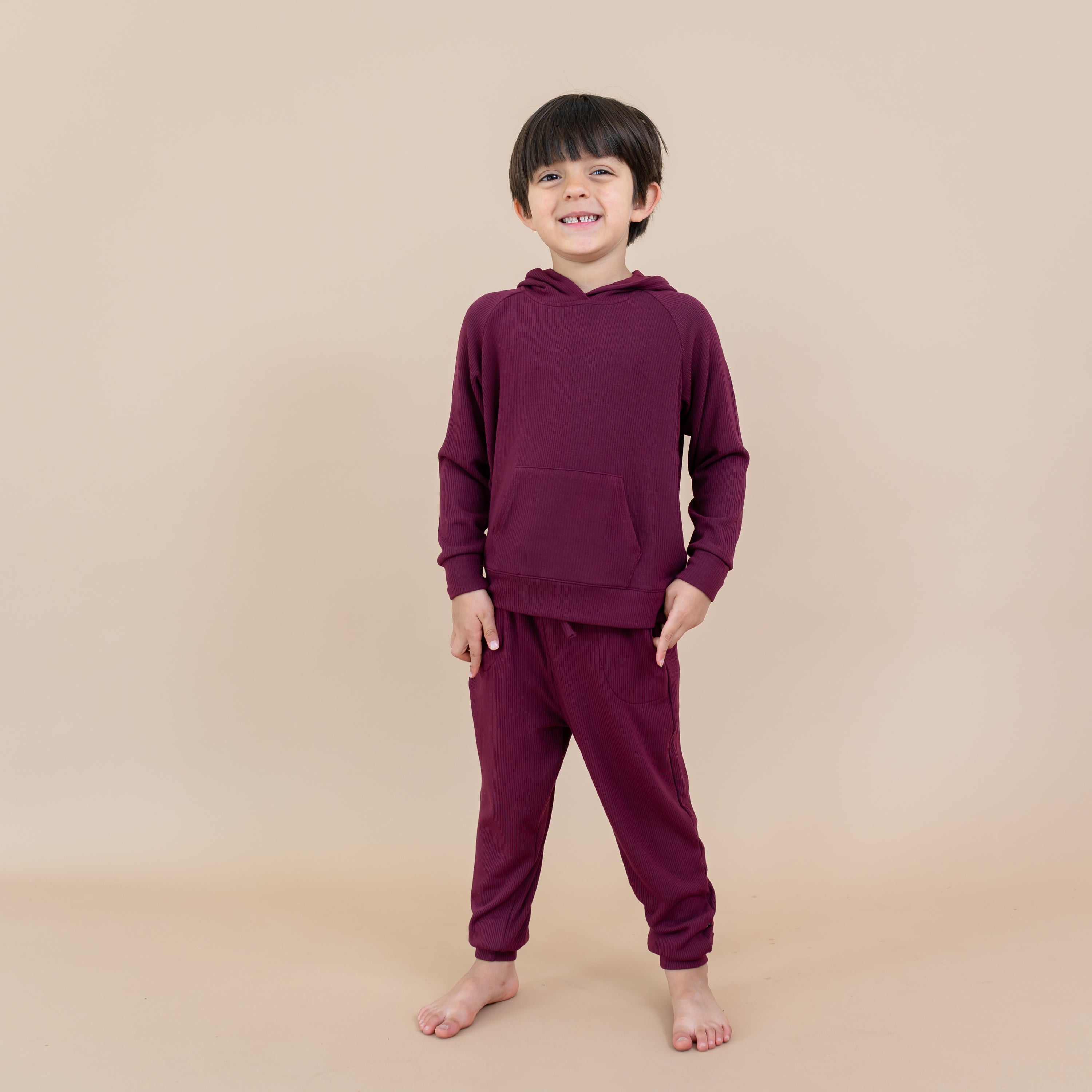 Child model smiling wearing the Ribbed Jogger Pant in Burgundy paired with a matching ribbed hoodie