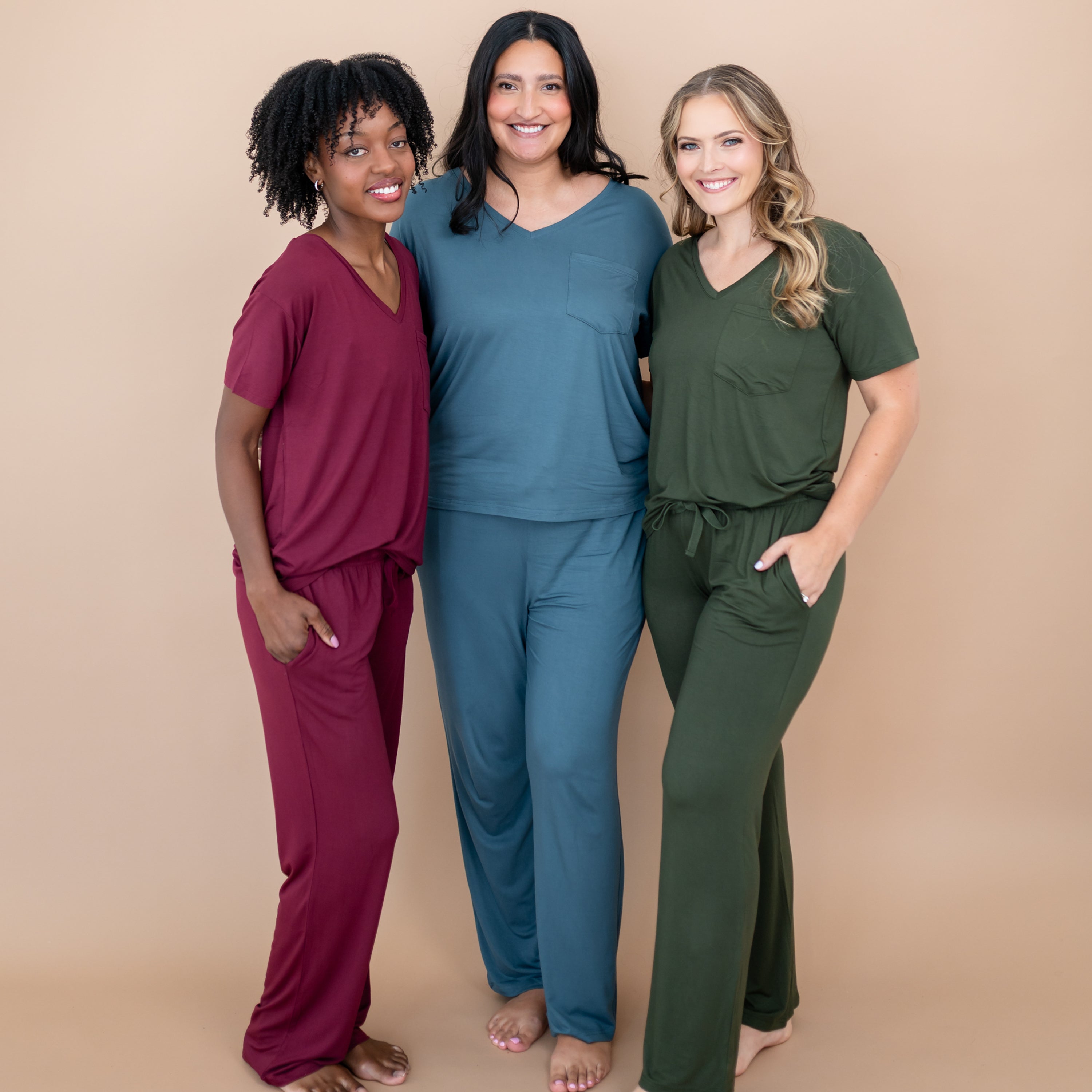 Three women standing side by side wearing the Women's Lounge Pants in Burgundy, Atlantic and Fir with matching women's v-necks