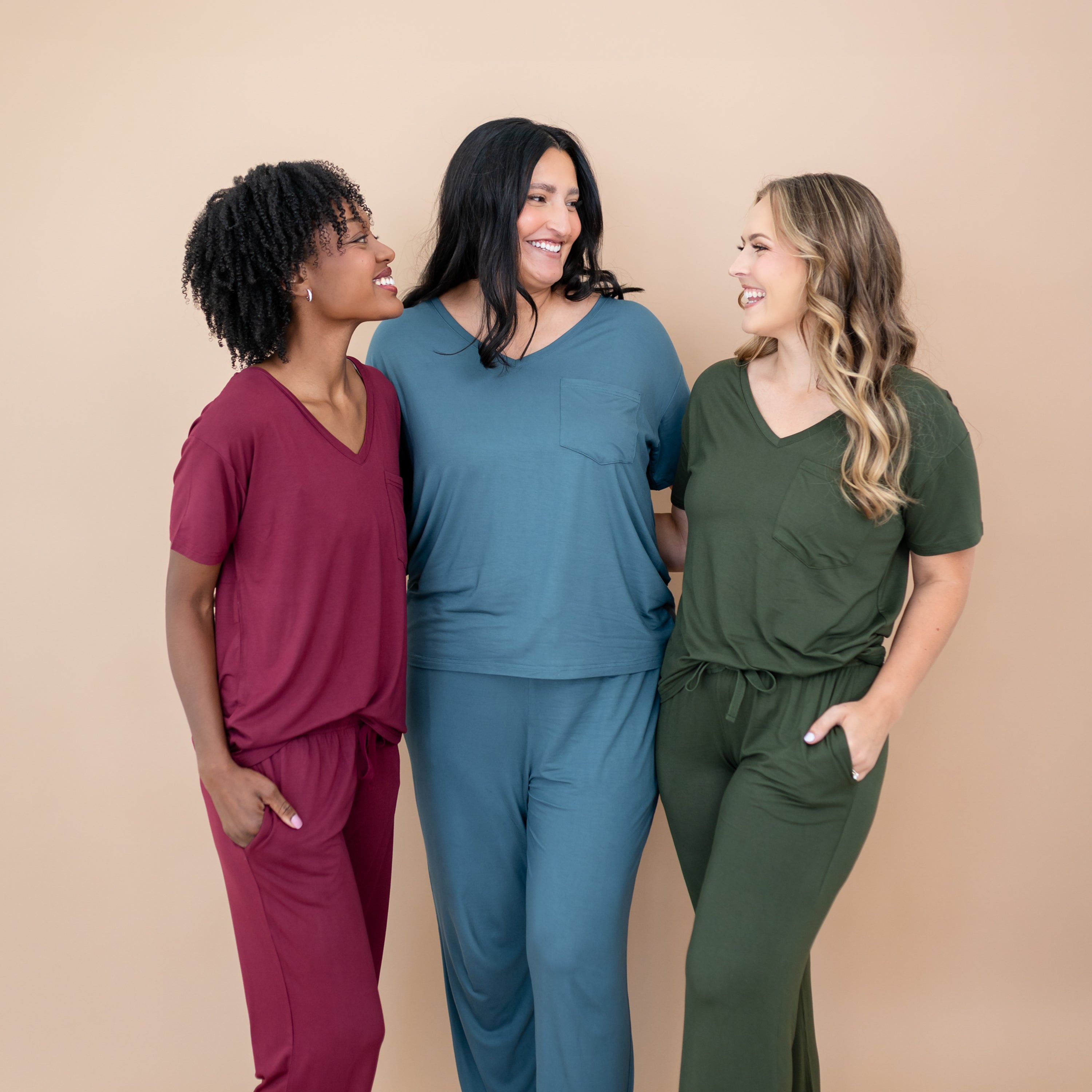 Group of three women wearing the Women’s Relaxed Fit V-Neck in Burgundy, Atlantic and Fir with matching lounge pants