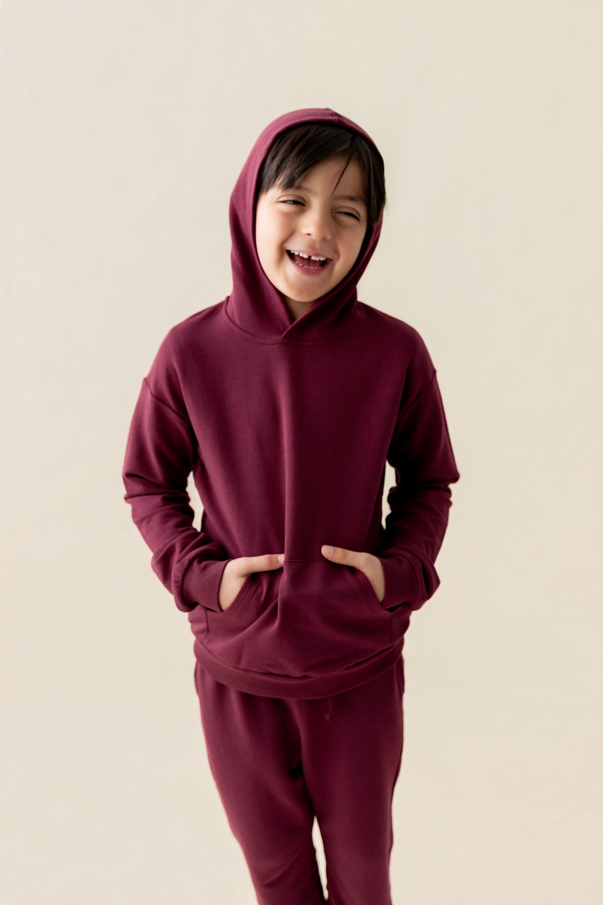 Boy smiling Hoodie in Burgundy color and similar color pants on a beige background