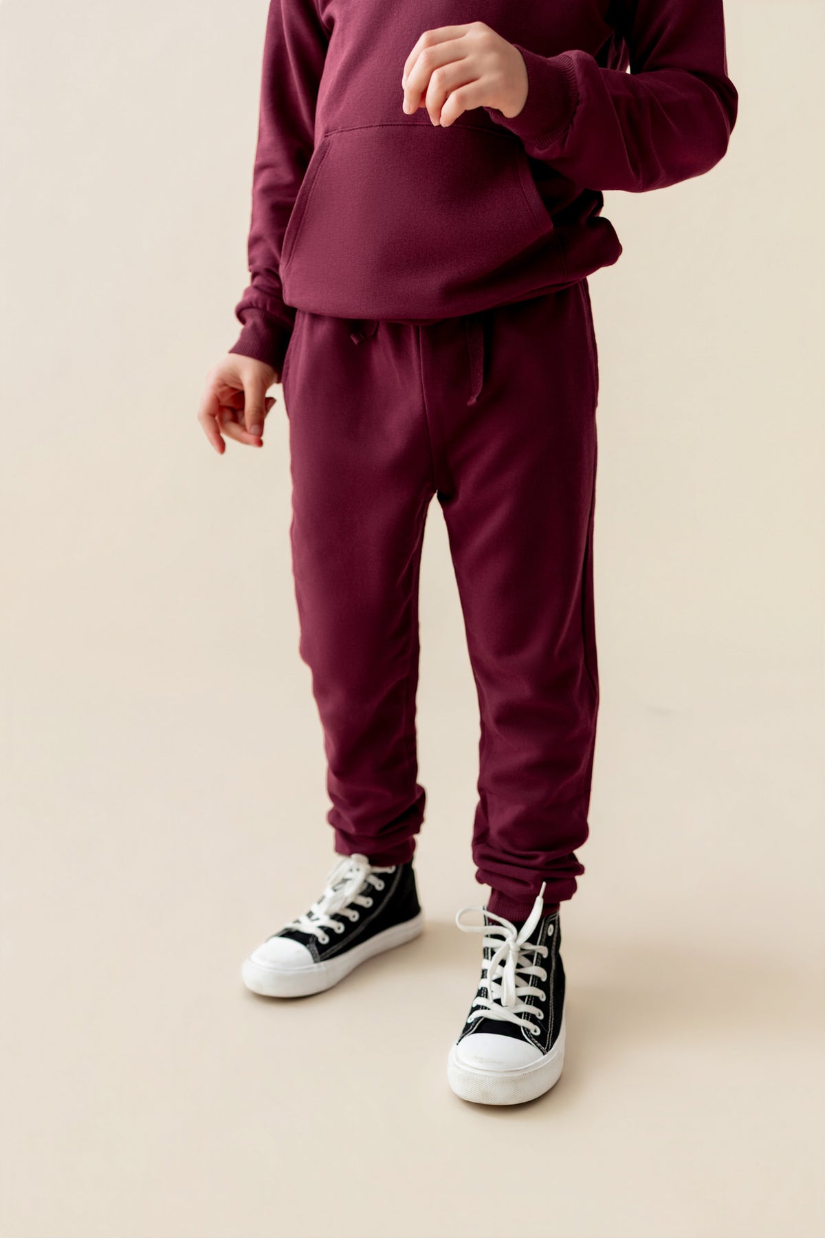 Modal wearing Jogger Pant in Burgundy color under burgundy color hoodie on a beige background