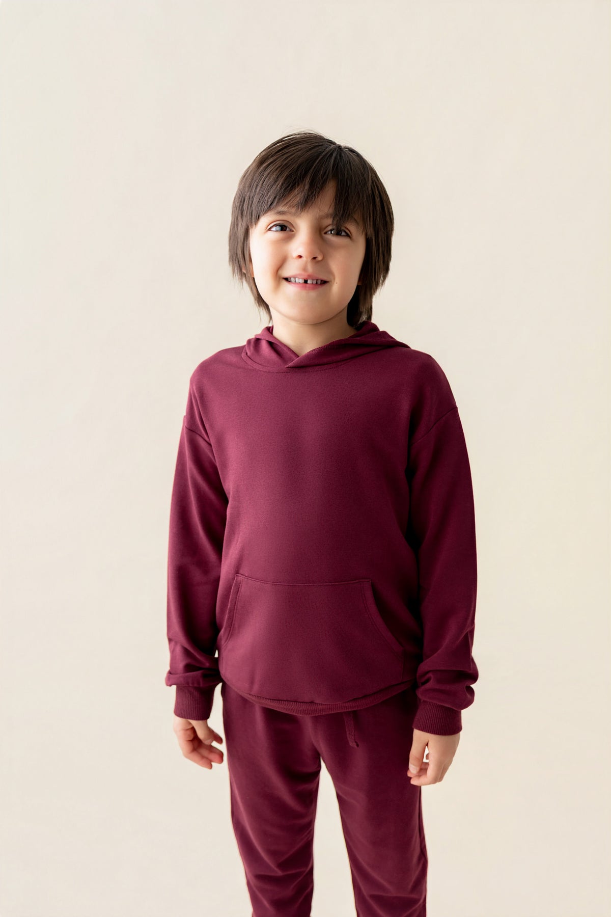 Boy wearing Hoodie in Burgundy color and similar color pants on a beige background