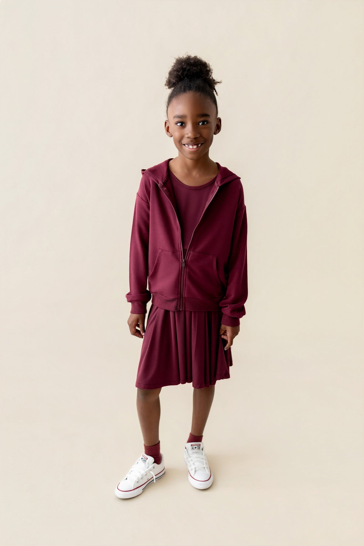 Girl wearing Zip-Up Hoodie in Burgundy color over long sleeve skater dress in burgundy on a beige background