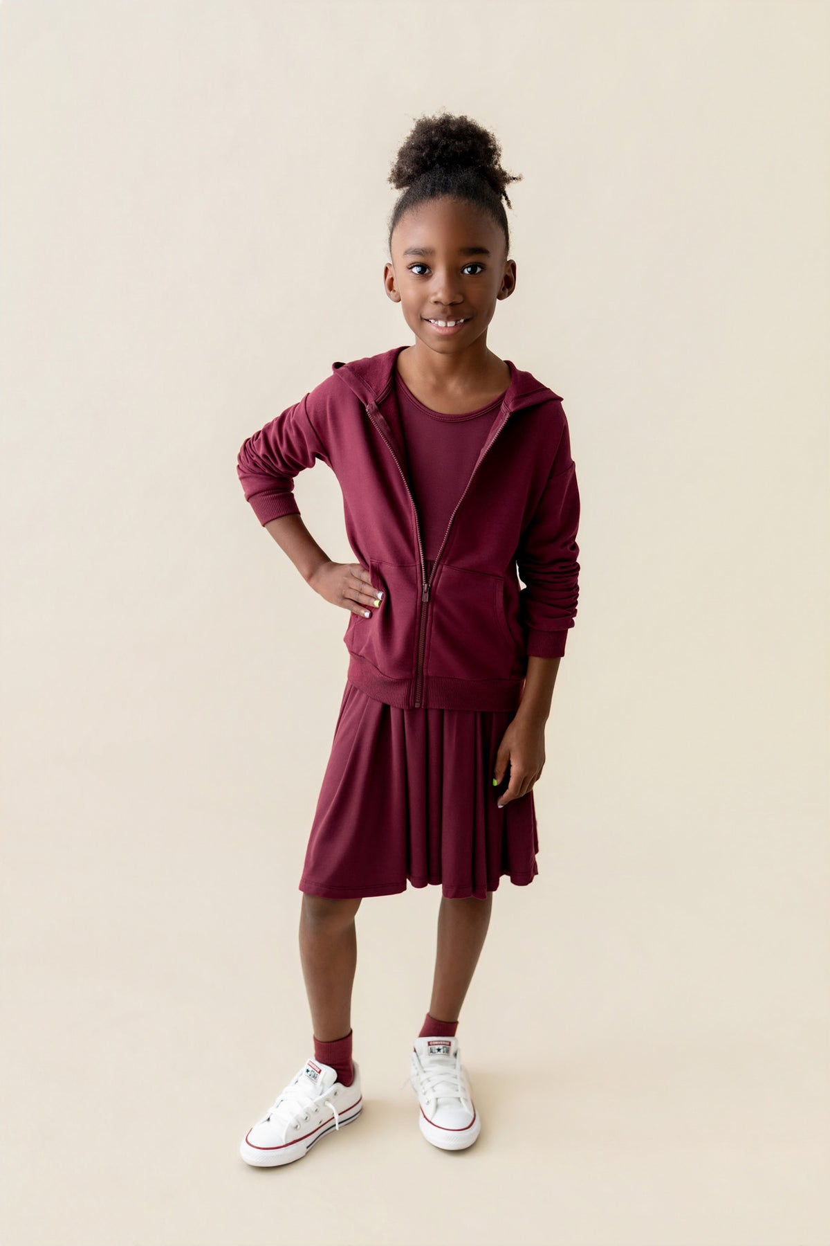 Girl wearing Zip-Up Hoodie in Burgundy color over long sleeve skater dress in burgundy and white shoes on a beige background