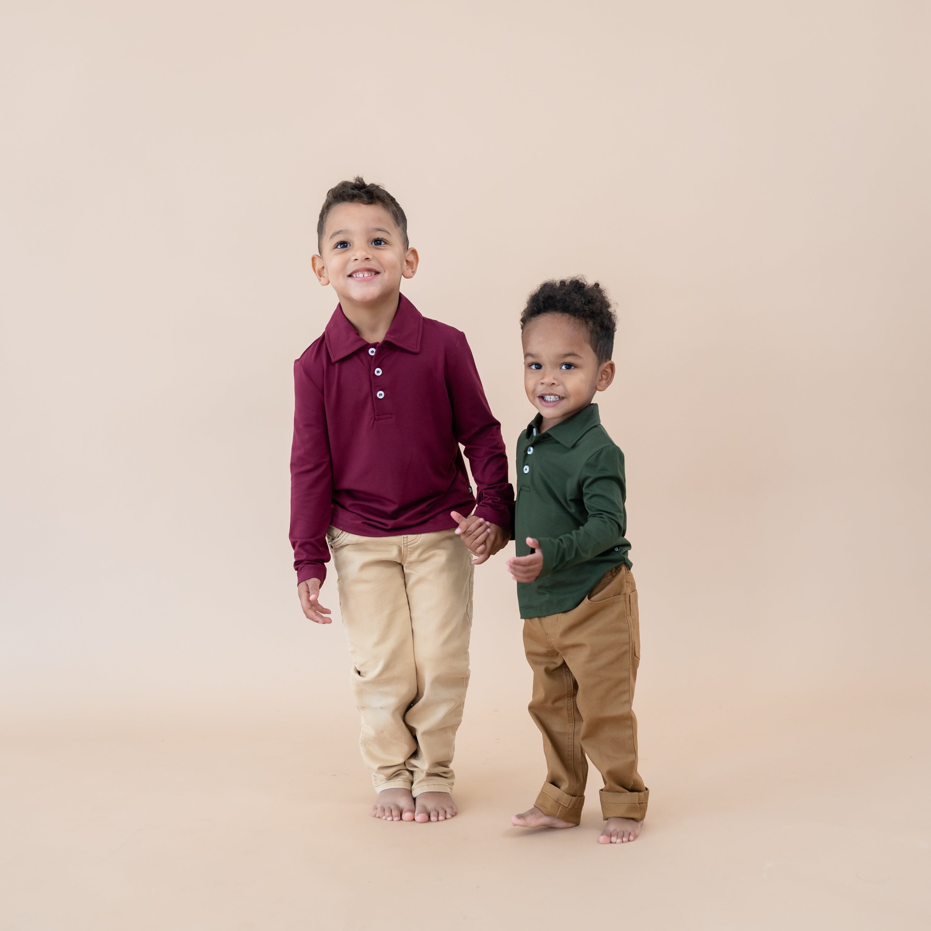 Two young boy models holding hands wearing the Toddler Long Sleeve Polo in Burgundy and Fir