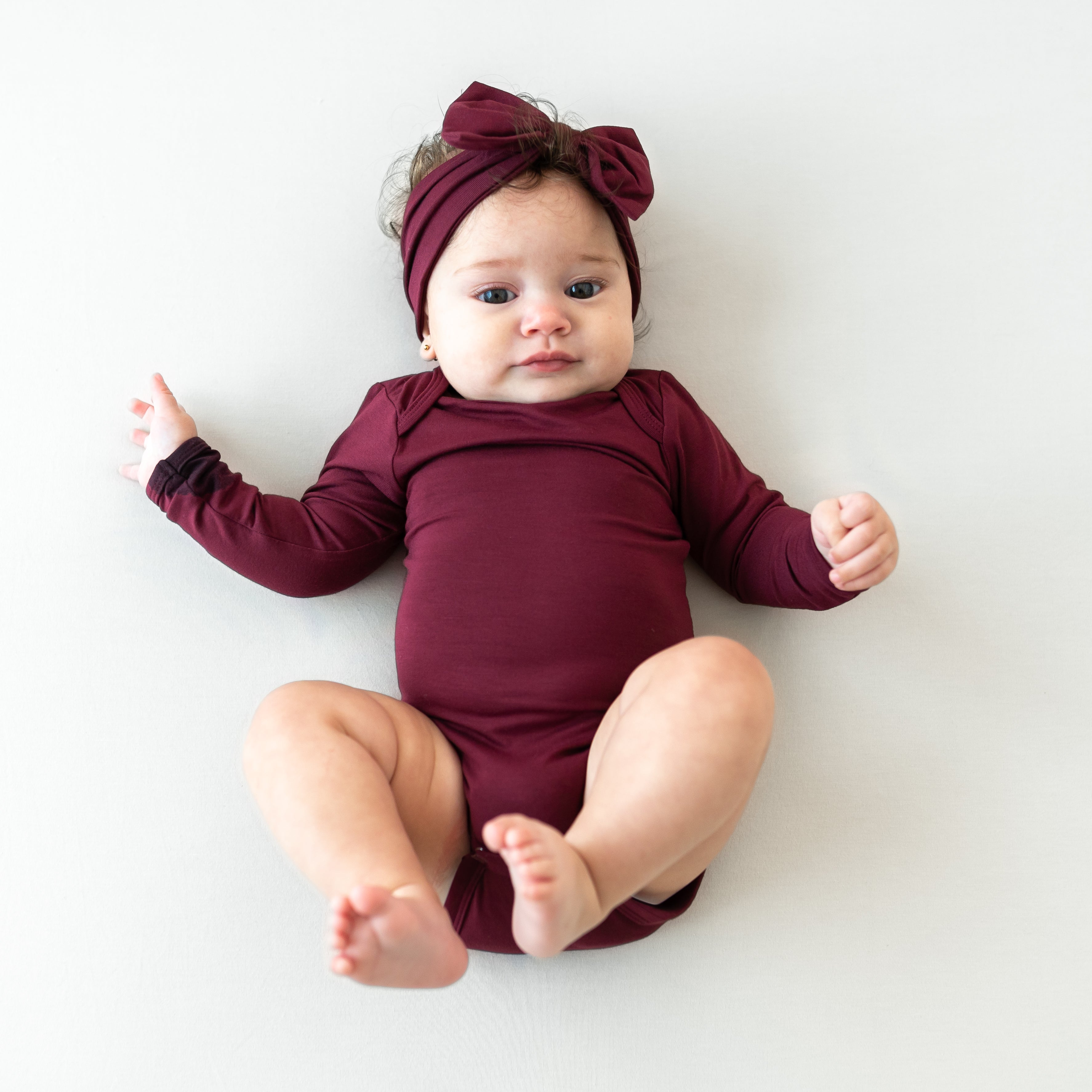 Infant laying down wearing the Bow Headband in Burgundy paired with matching long sleeve bodysuit