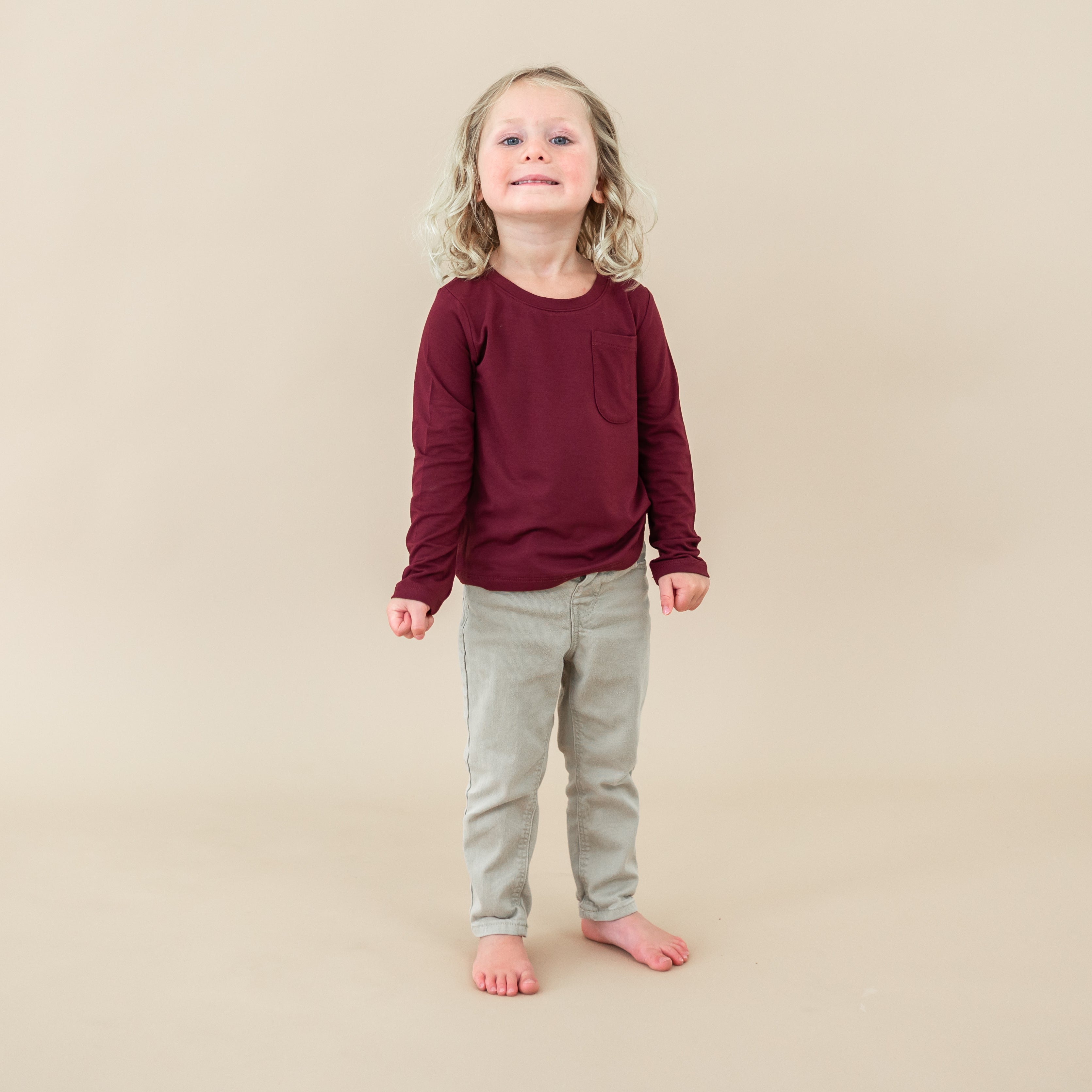 Smiling toddler wearing the Long Sleeve Toddler Crew Neck Tee in Burgundy and light colored jeans