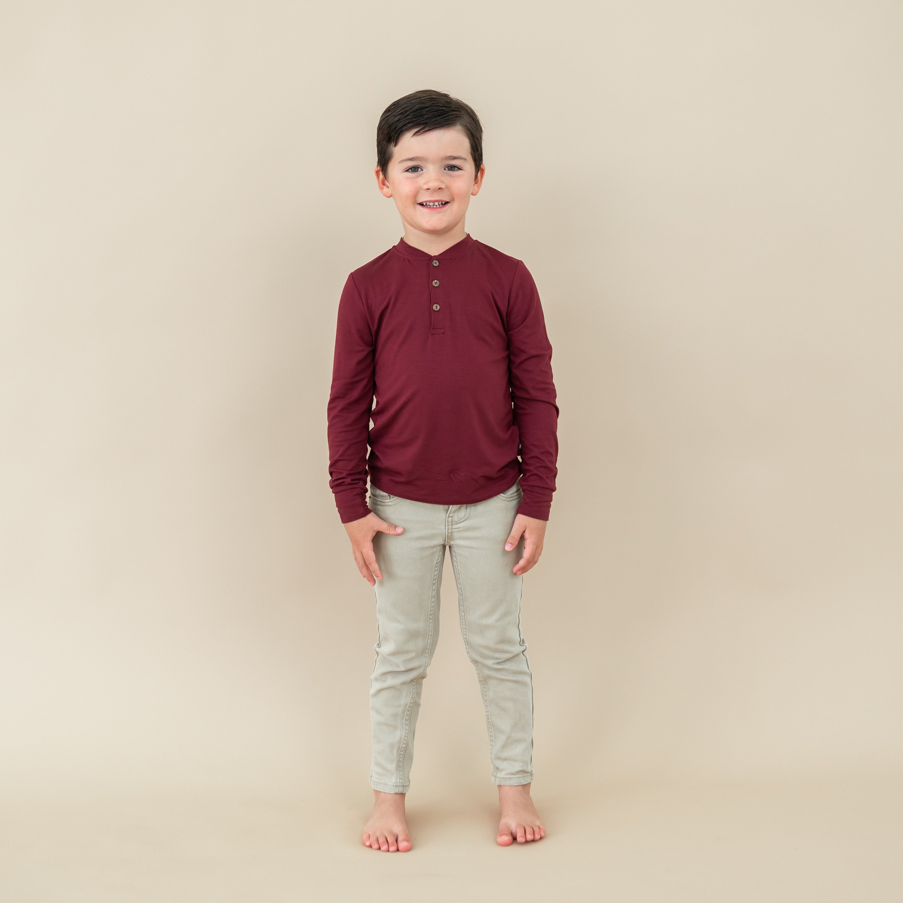 Young boy model standing wearing the Long Sleeve Toddler Henley Tee in Burgundy paired with light colored jeans