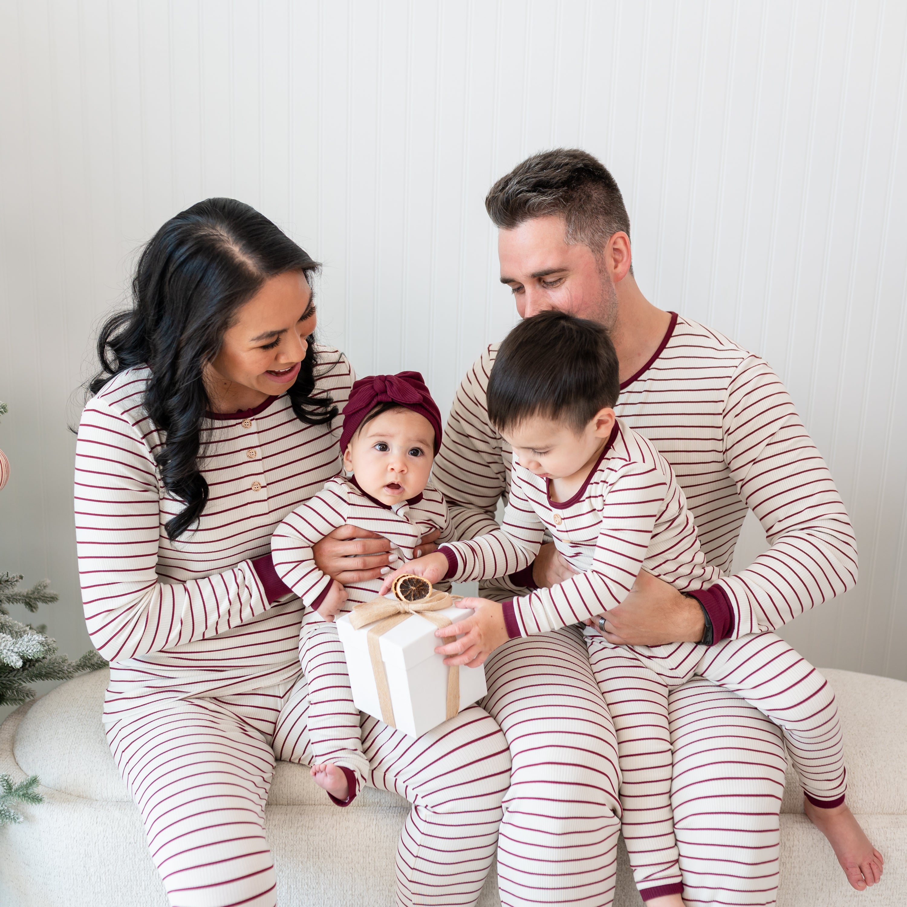 Family of four sitting on a cream ottoman matching in Burgundy Stripe items