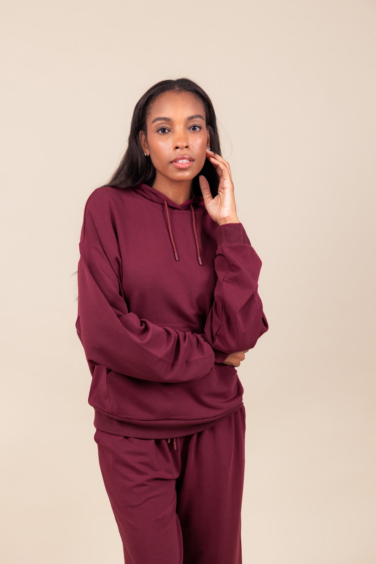 Woman posing in Women's Hoodie in Burgundy color over similar color women's sweatpants on a beige background