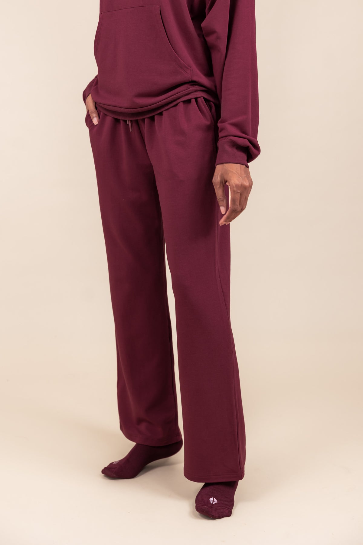 Close up of Modal wearing Women's Sweatpants in Burgundy color with pockets under similar color hoodie on a beige background