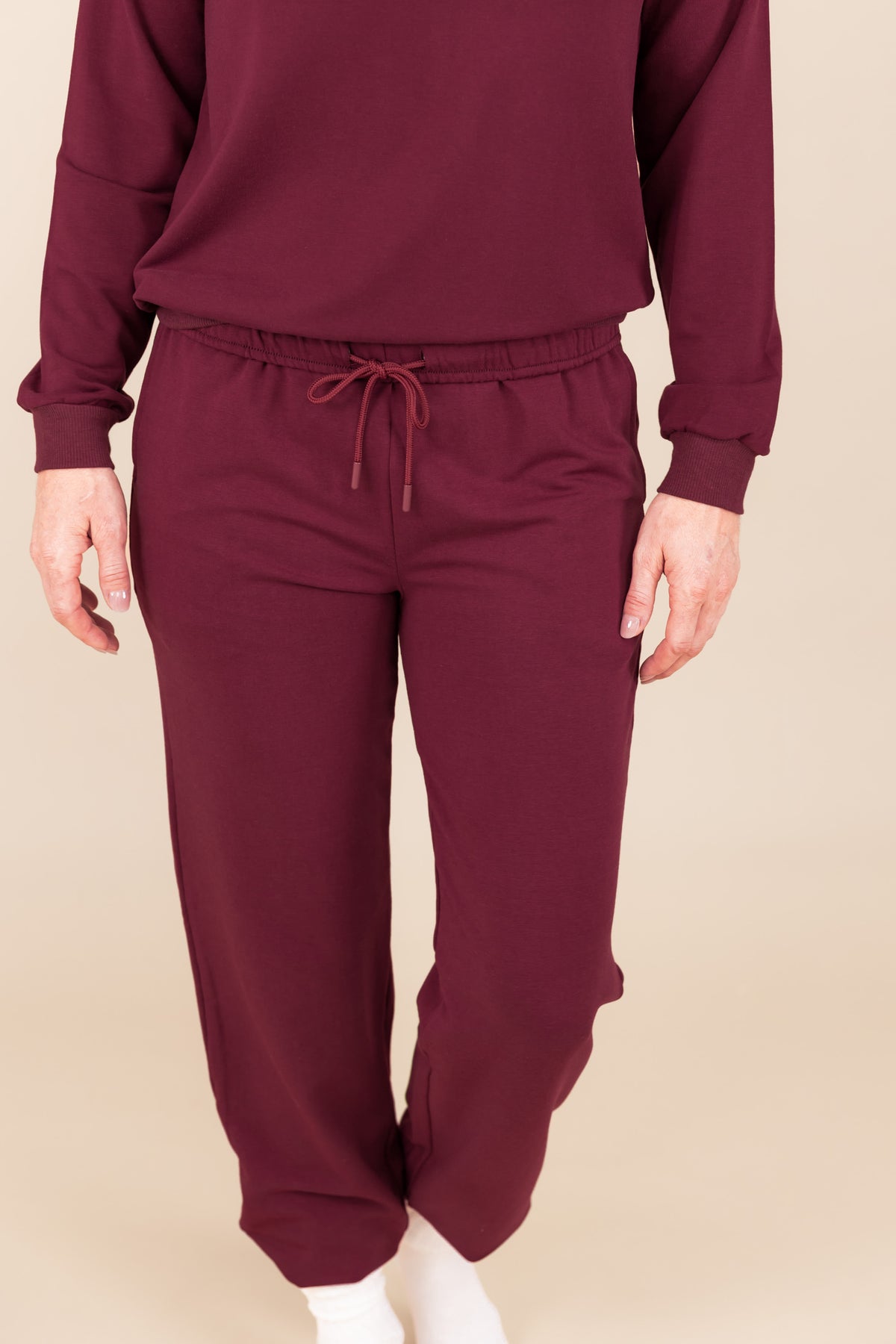 Modal wearing Women's Jogger Pant in Burgundy color under similar color sweatshirt on a beige background