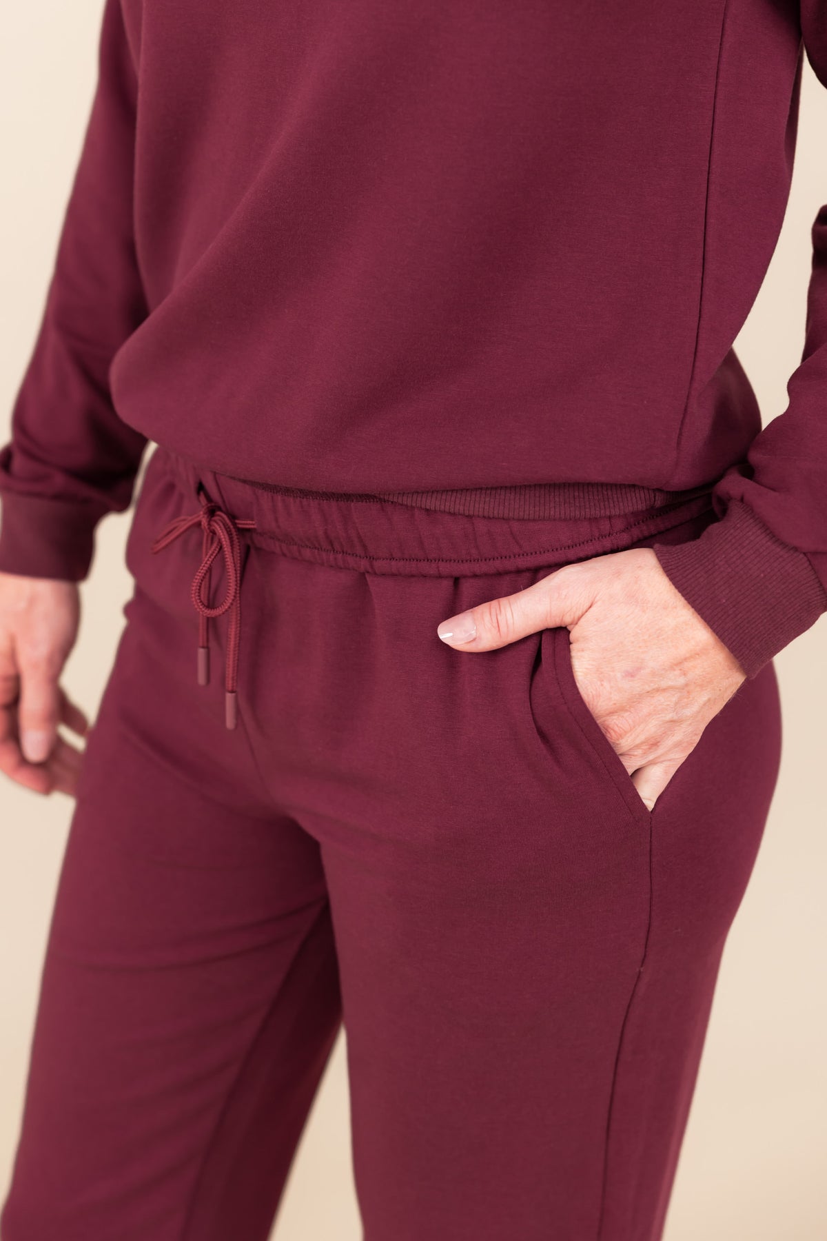 Modal wearing Women's Jogger Pant in Burgundy color with pockets under similar color sweatshirt on a beige background