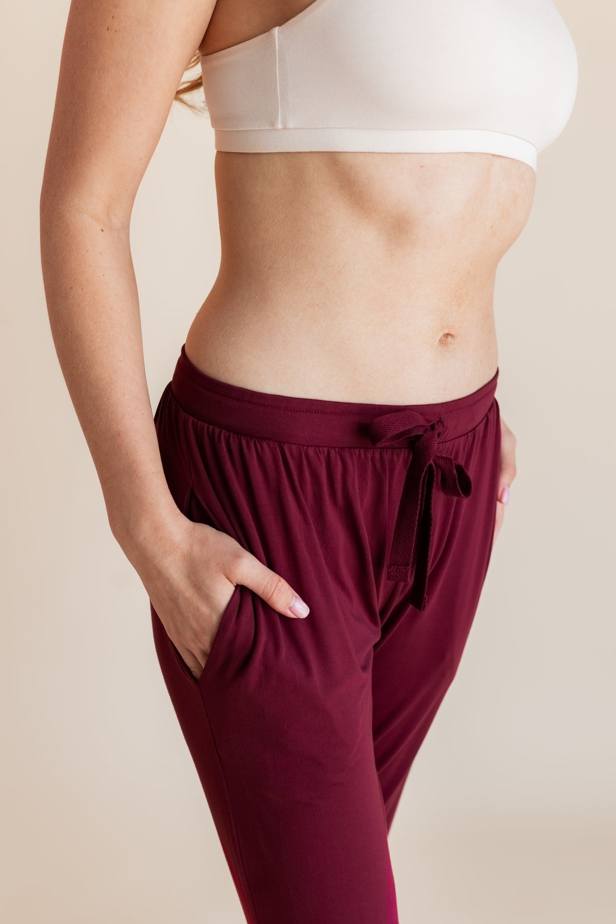 Model showcasing pockets on Women's Jogger Pants in Burgundy under white bralette on a beige background