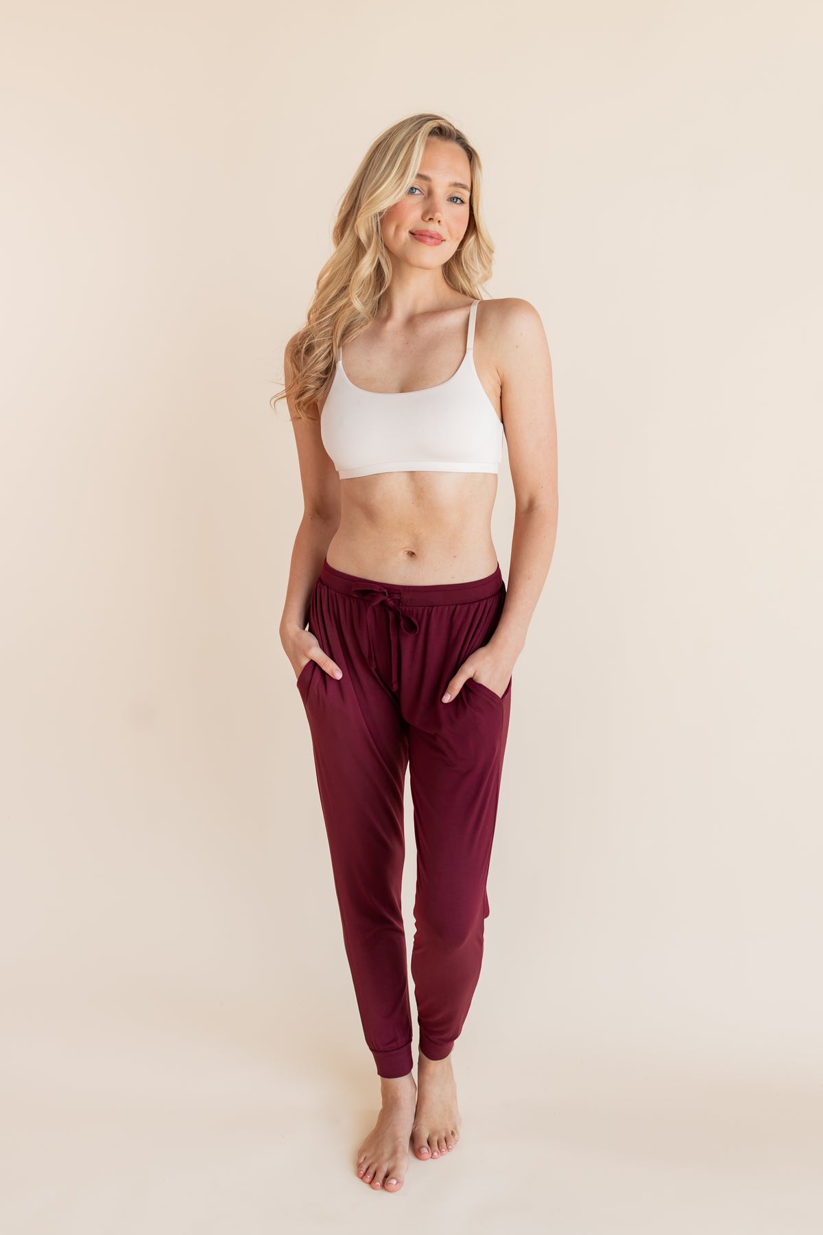 Model wearing Women's Jogger Pants in Burgundy with pockets under white bralette on a beige background
