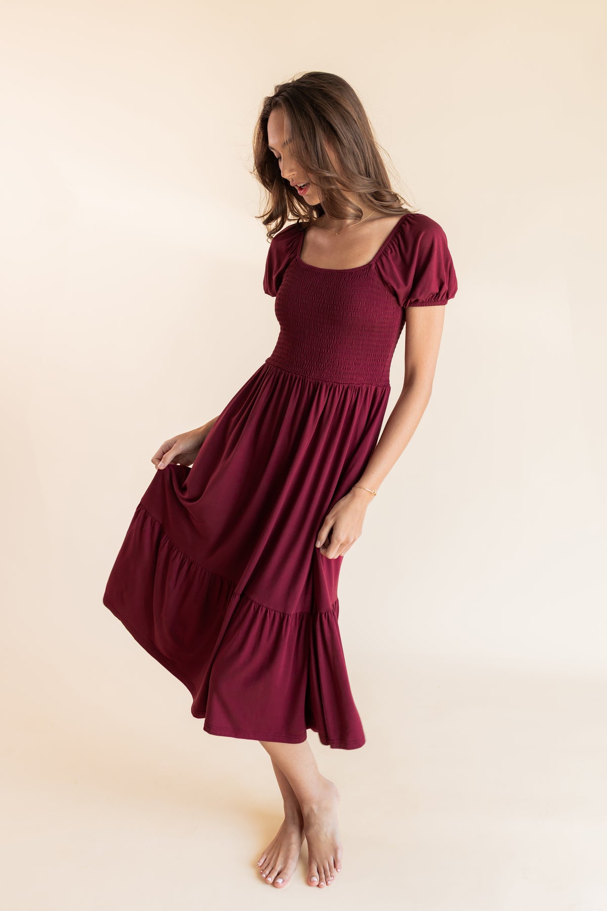 Model moving Women’s Smocked Dress in Burgundy on a beige background