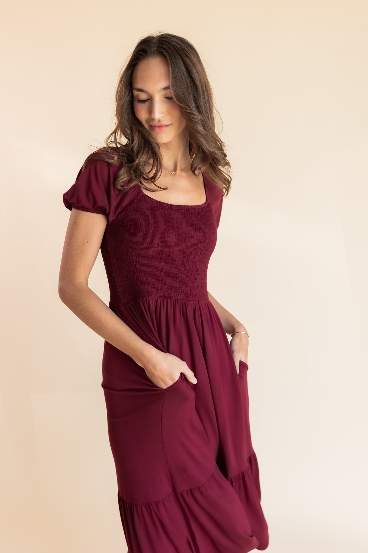 Model posing in Women’s Smocked Dress in Burgundy with pockets on a beige background