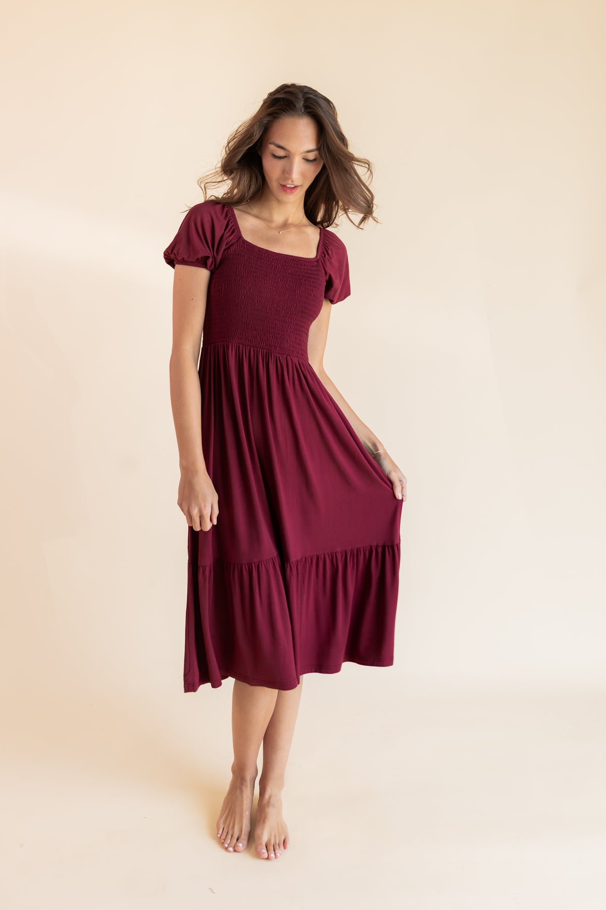 Model wearing Women’s Smocked Dress in Burgundy on a beige background
