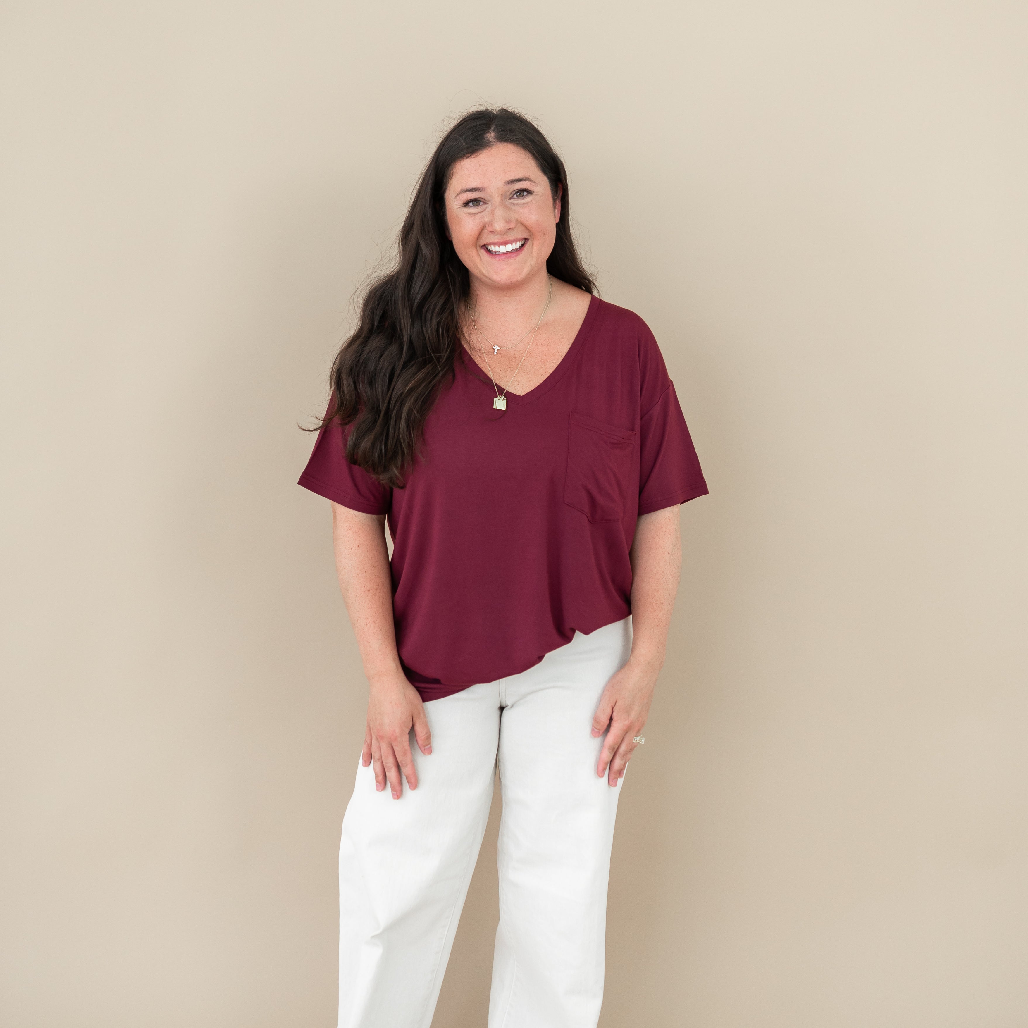Smiling model standing with hands at her side wearing the Women’s Relaxed Fit V-Neck in Burgundy paired with cream pants