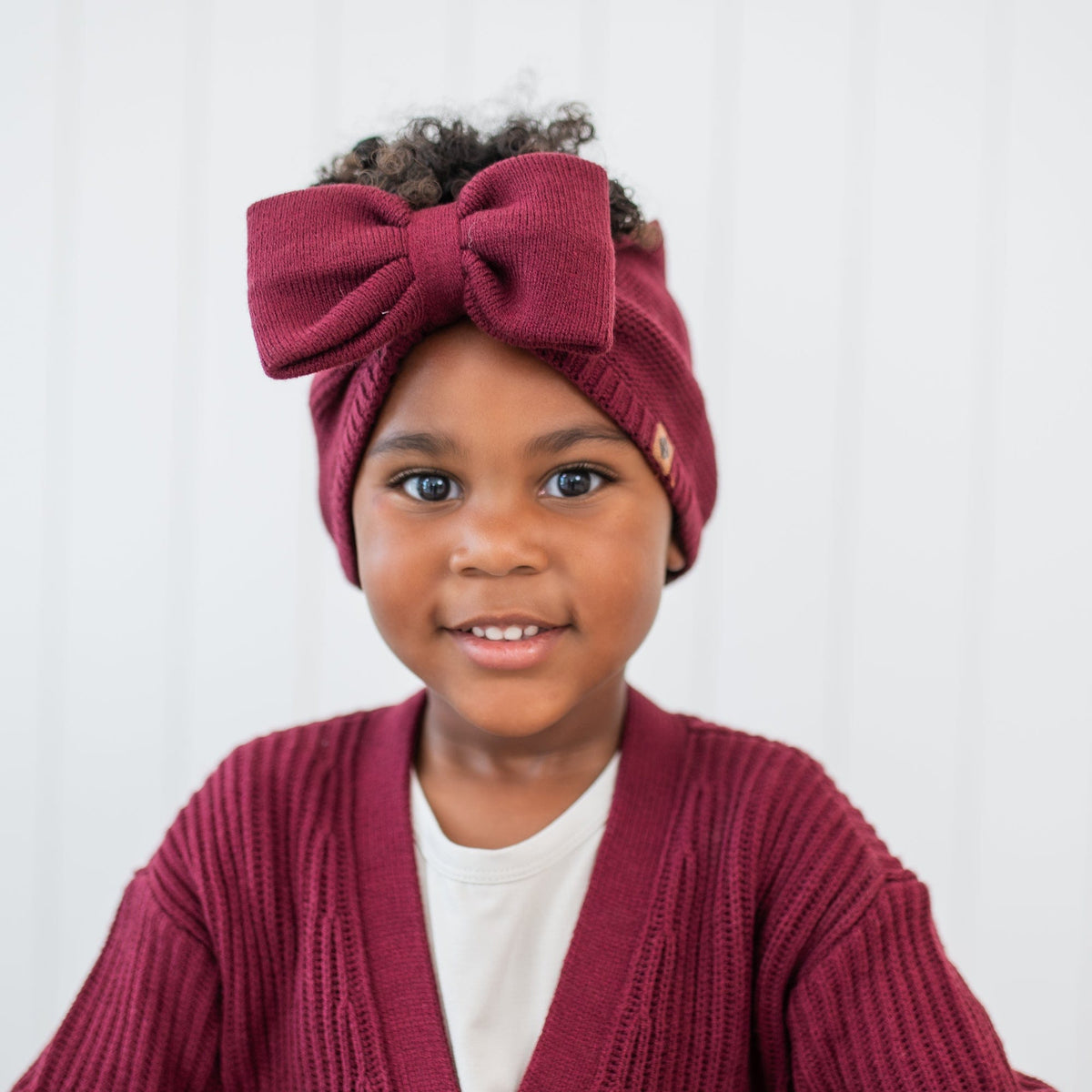 Close up of the Chunky Knit Bow Headband in Burgundy shown on a young girl