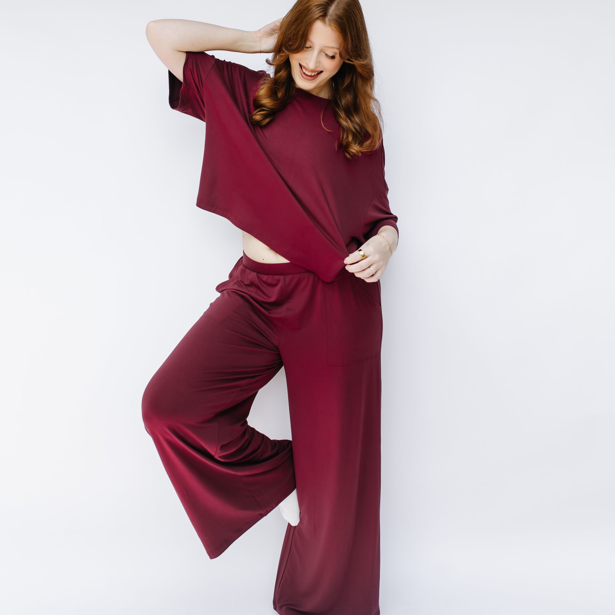 Female model posing with one arm behind her head and one leg bent resting against her opposite knee wearing the Women's Wide Leg Pant in Burgundy and matching short sleeve tee