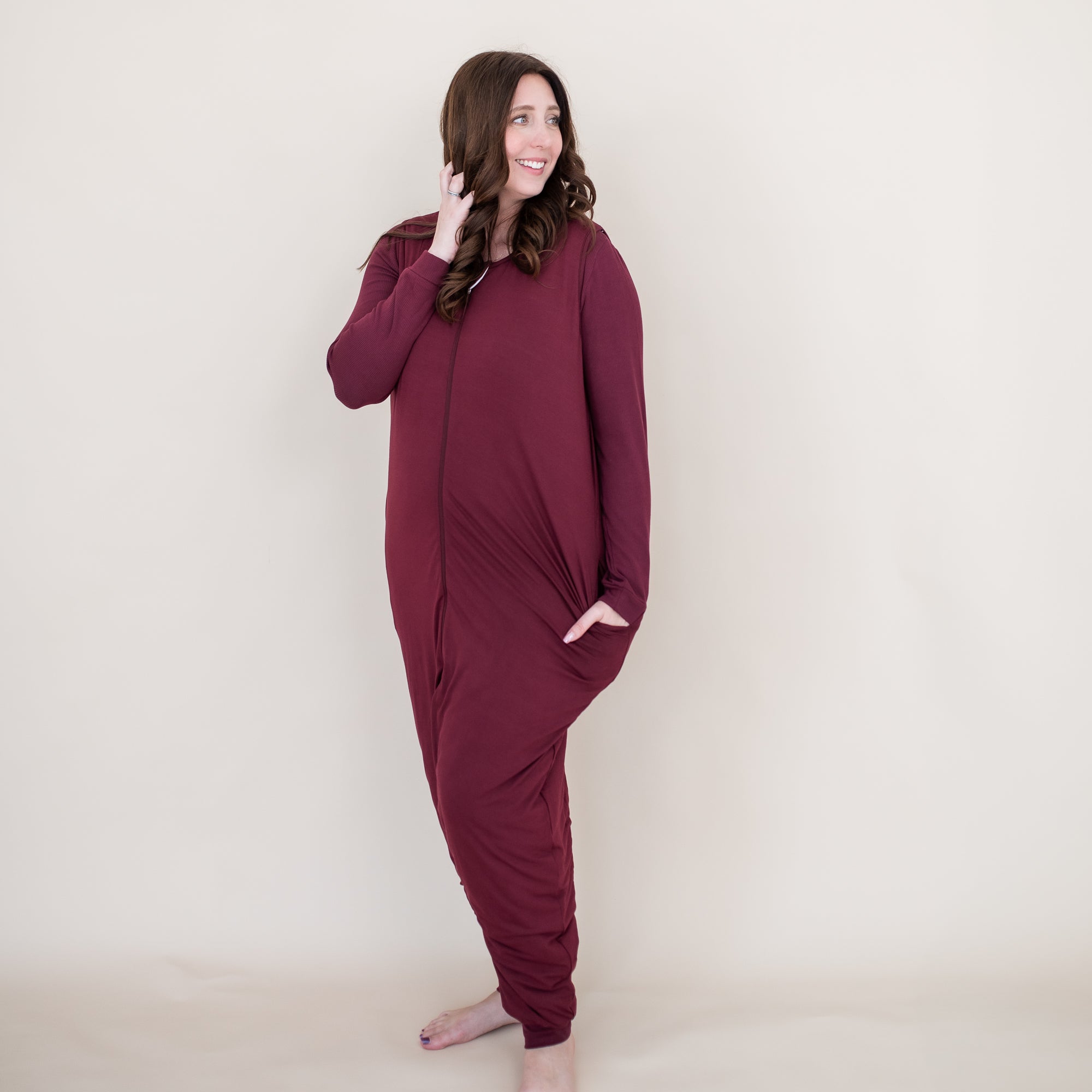 Smiling female standing with one hand in her hair and the other hand in the pocket of the Adult Sleep Bag Walker in Burgundy