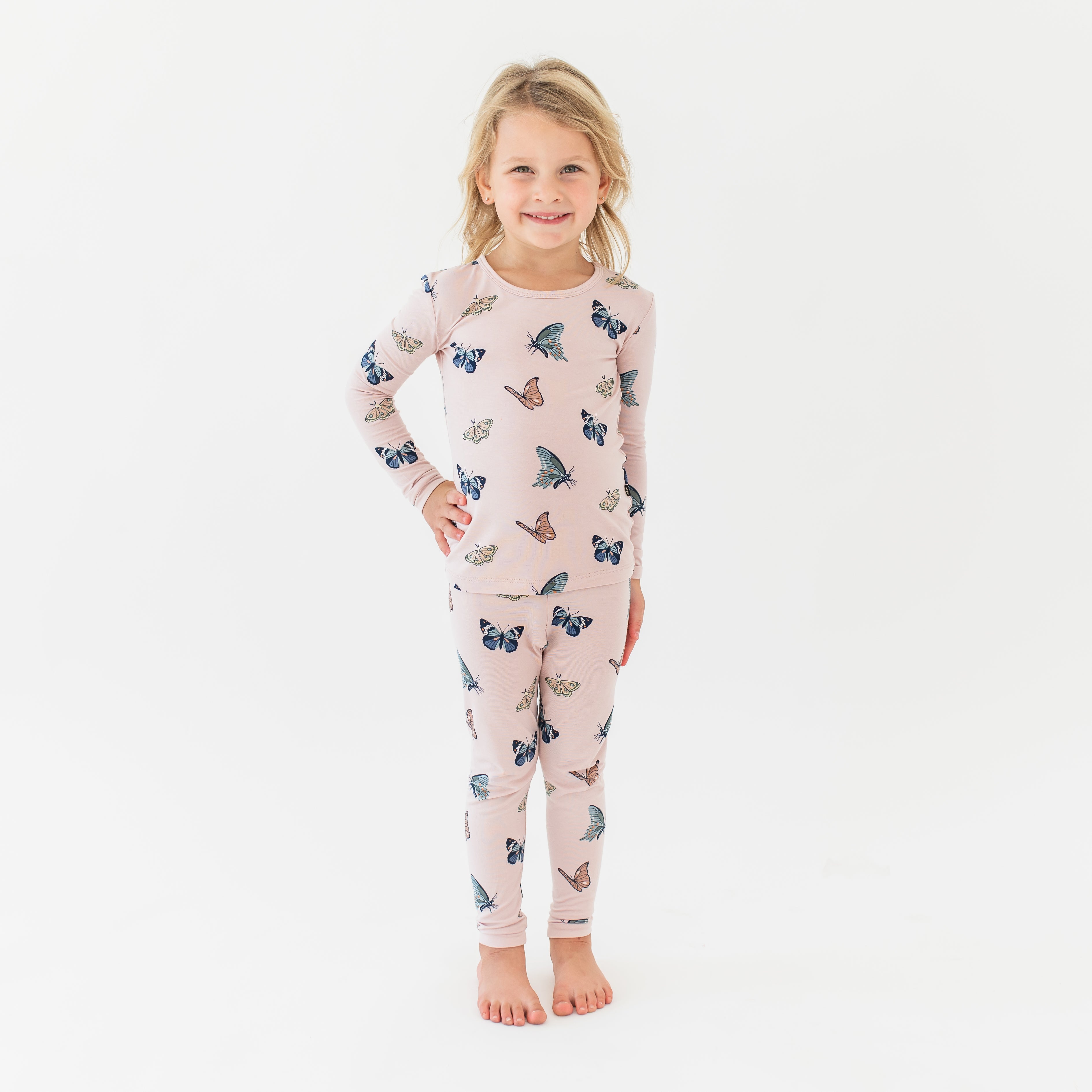 Young girl standing with her hand on her hip wearing the Long Sleeve Pajamas in Blush Butterfly in front of a white background