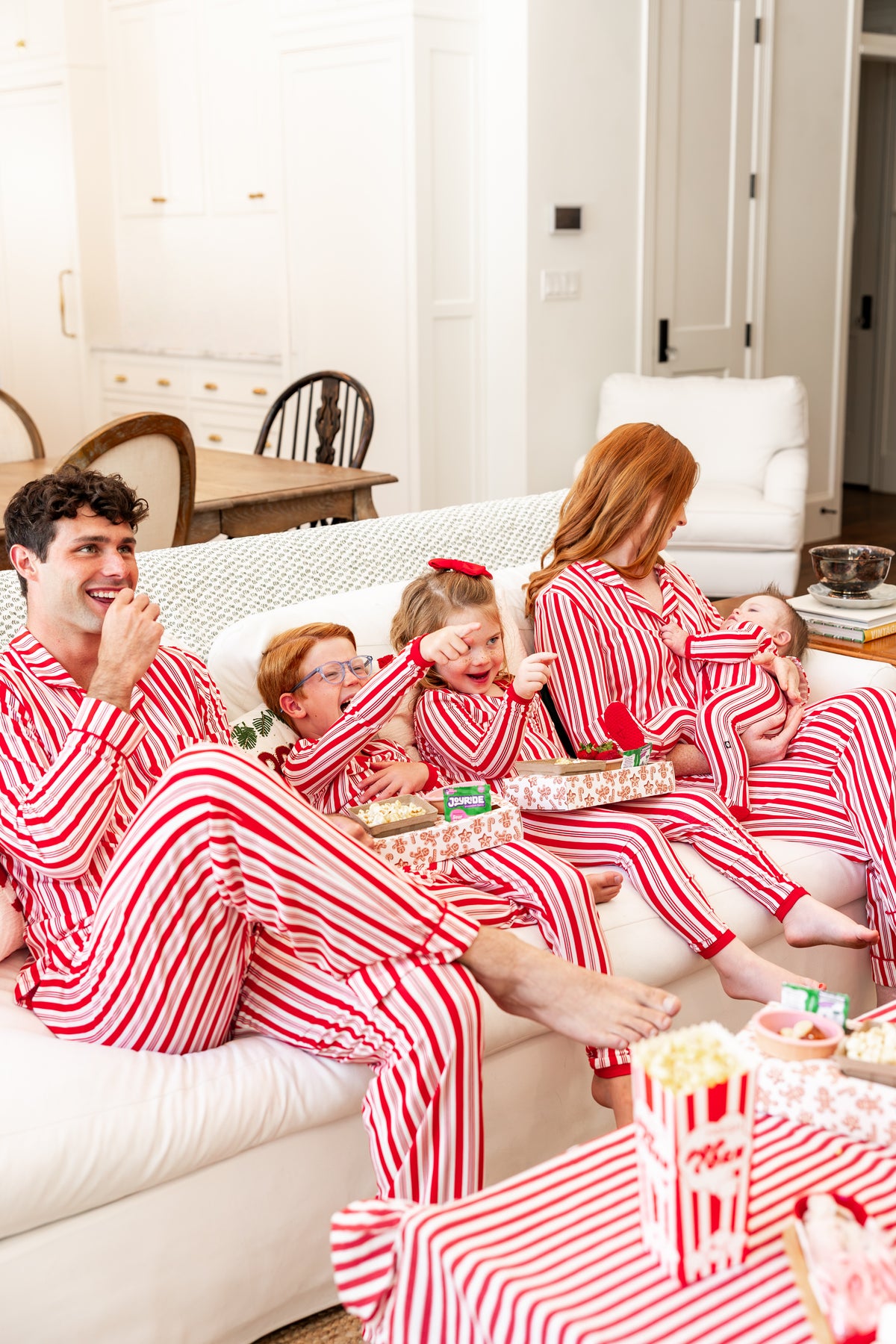 Family of 5 wearing matching red peppermint striped pajamas snuggled on a couch
