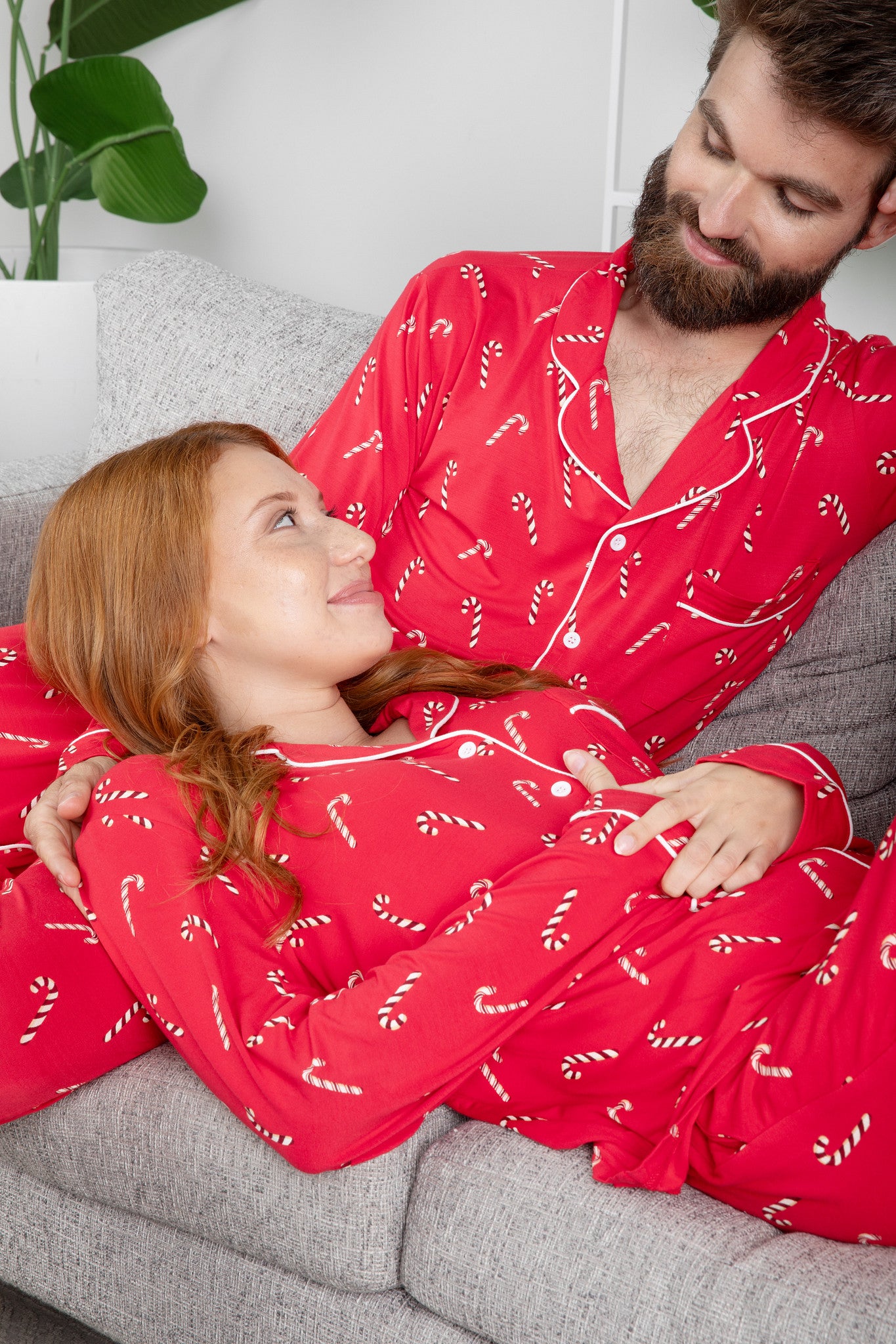 Wife laying on husbands lap both on the couch matching in Men's and Women's Long Sleeve Pajama Set in Candy Cane
