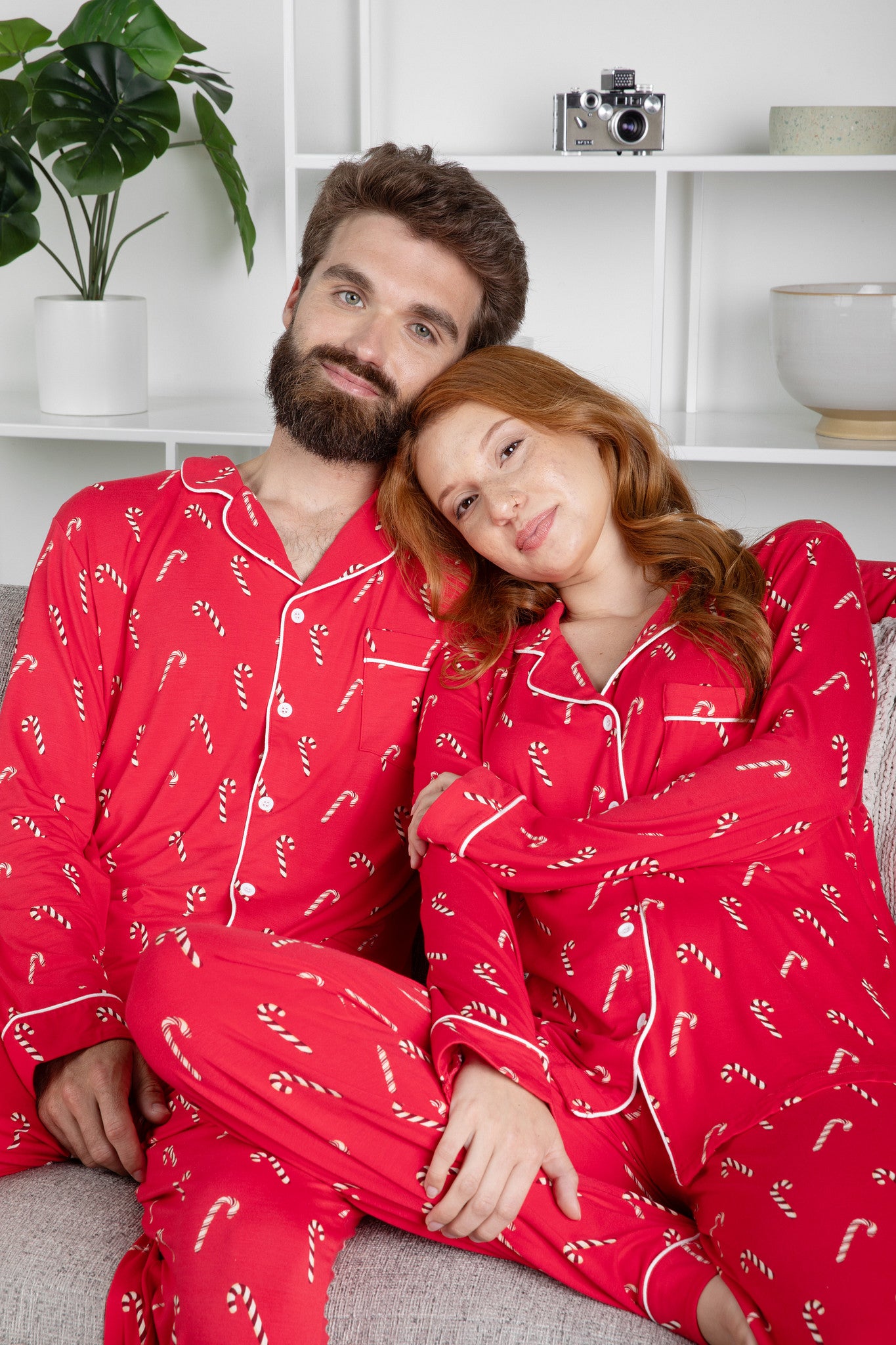 Husband and wife sitting on a couch matching in Men's and Women's Long Sleeve Pajama Set in Candy Cane
