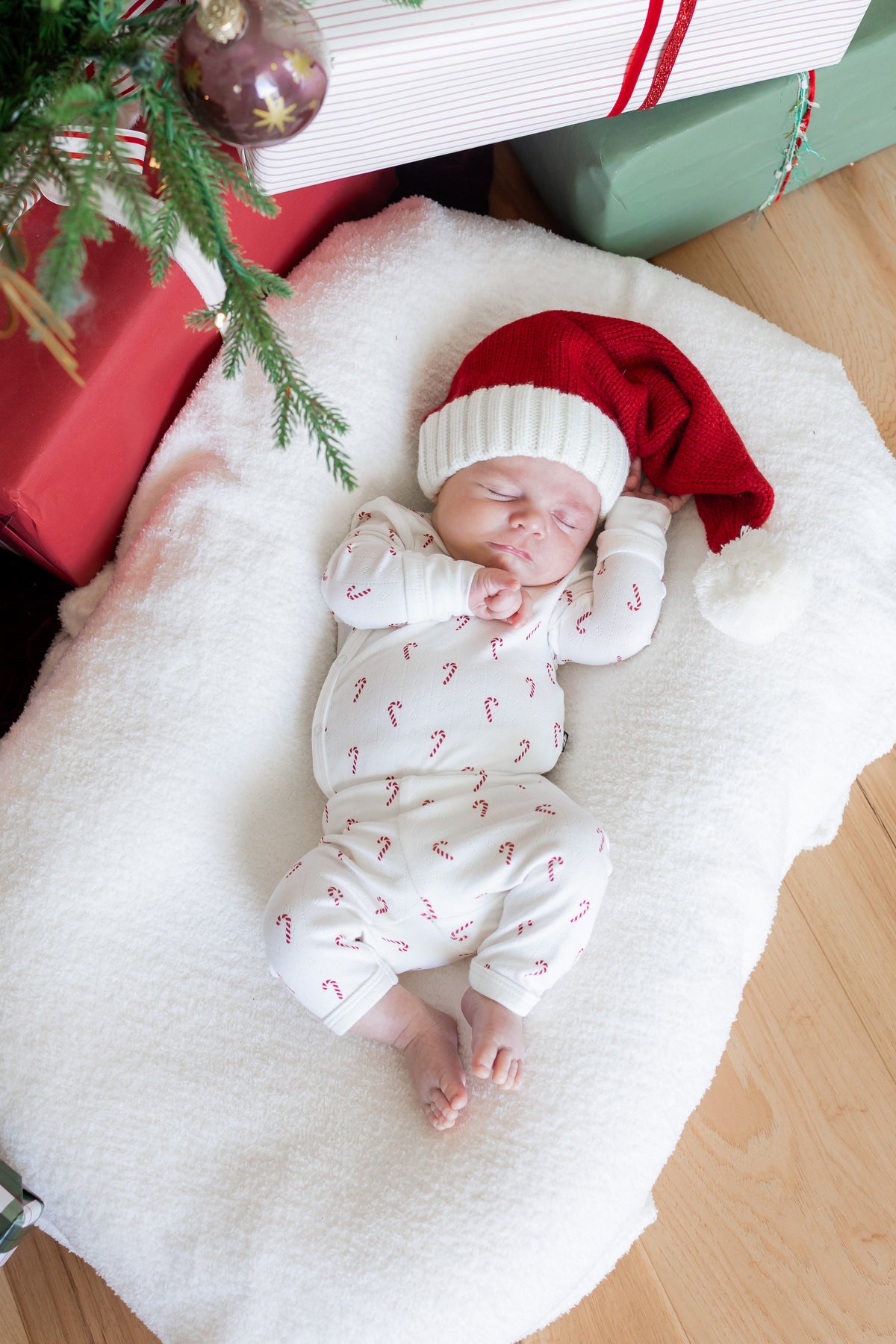 Baby sleeping wearing Pointelle Kimono Set in Candy Cane and red hat on a white sheet near presents