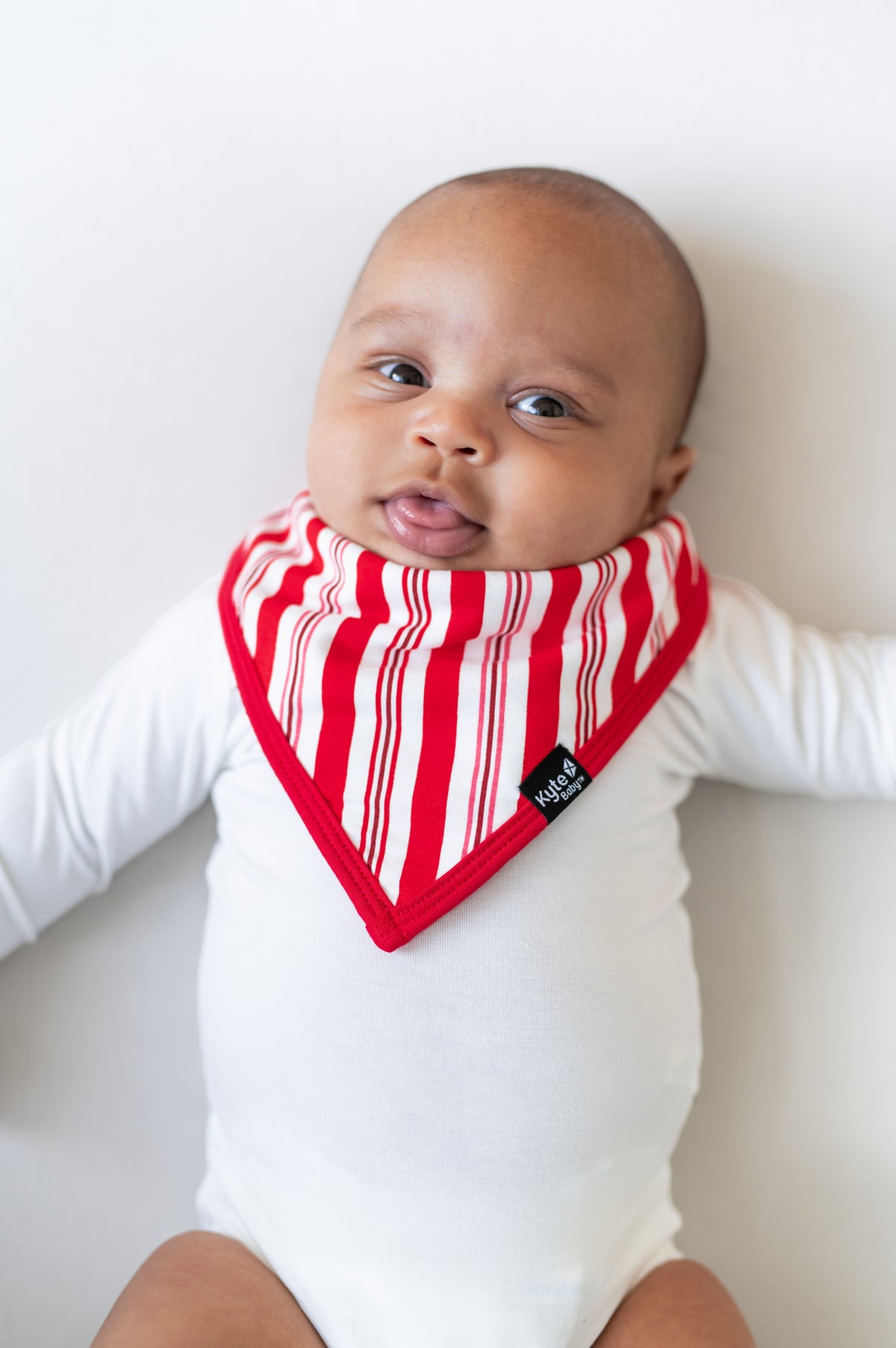 Baby wearing Bib in red and white Peppermint Stripes print over a white bodysuit on a white background