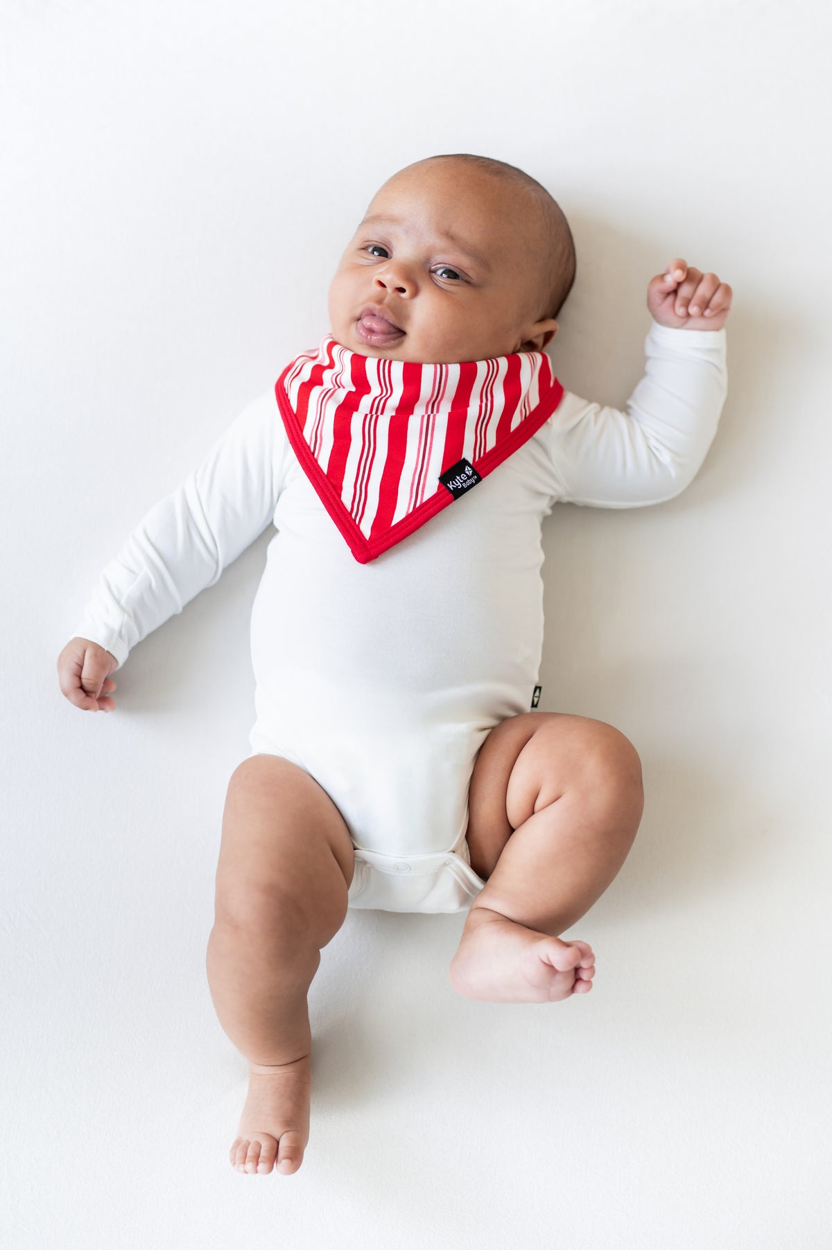 Baby wearing Bib in red and white Peppermint Stripes print over a white bodysuit on a white background