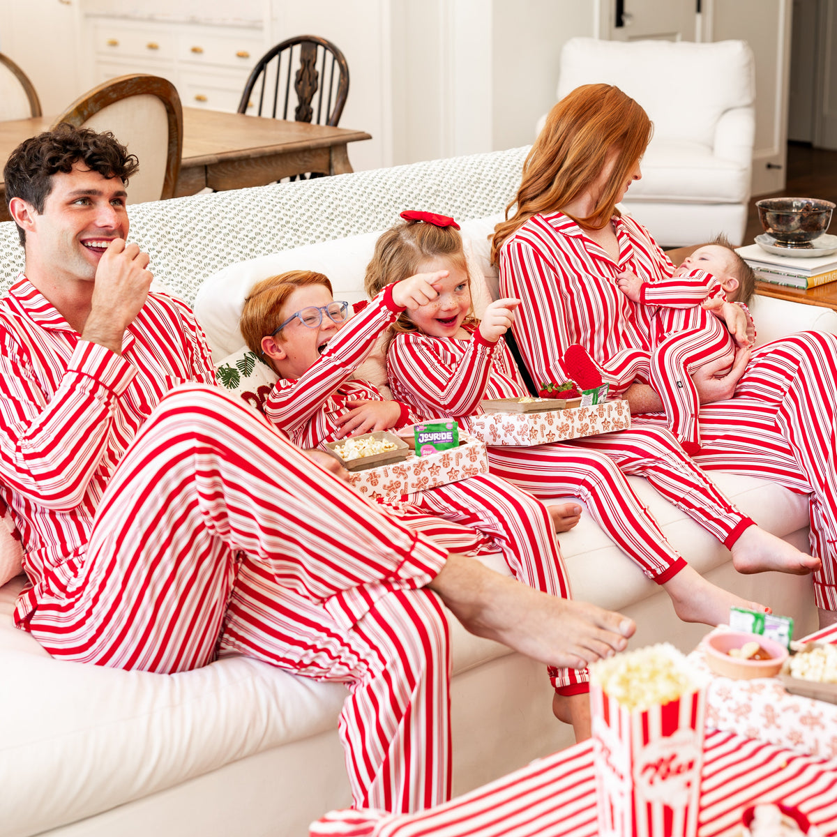 family of 5 sitting on couch wearing matching peppermint stripe pajamas