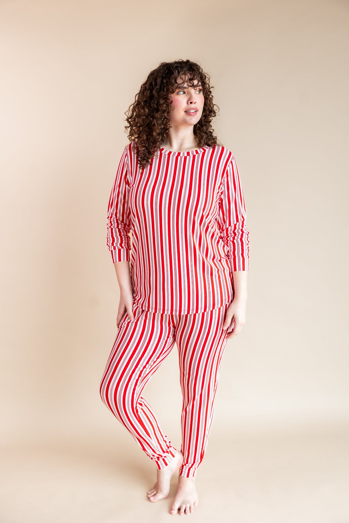 Woman posing in Women's Jogger Pajama Set in red and white Peppermint Stripes print on a beige background