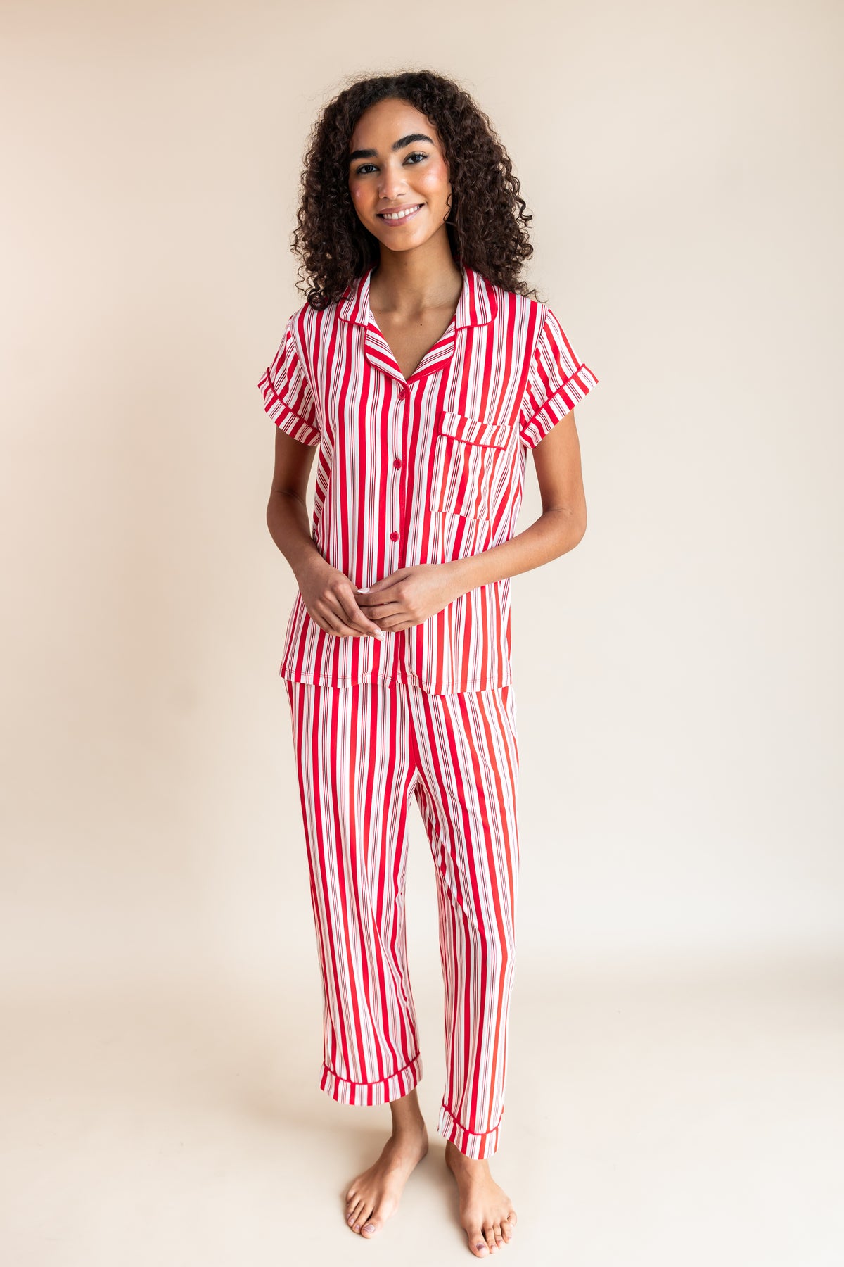 Modal wearing Women's Short Sleeve Cropped Pajama Set in red and white Peppermint Stripes print on a beige background