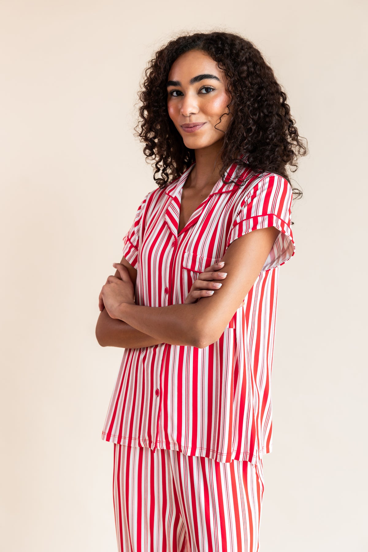 Modal posing in Women's Short Sleeve Cropped Pajama Set in red and white Peppermint Stripes print on a beige background
