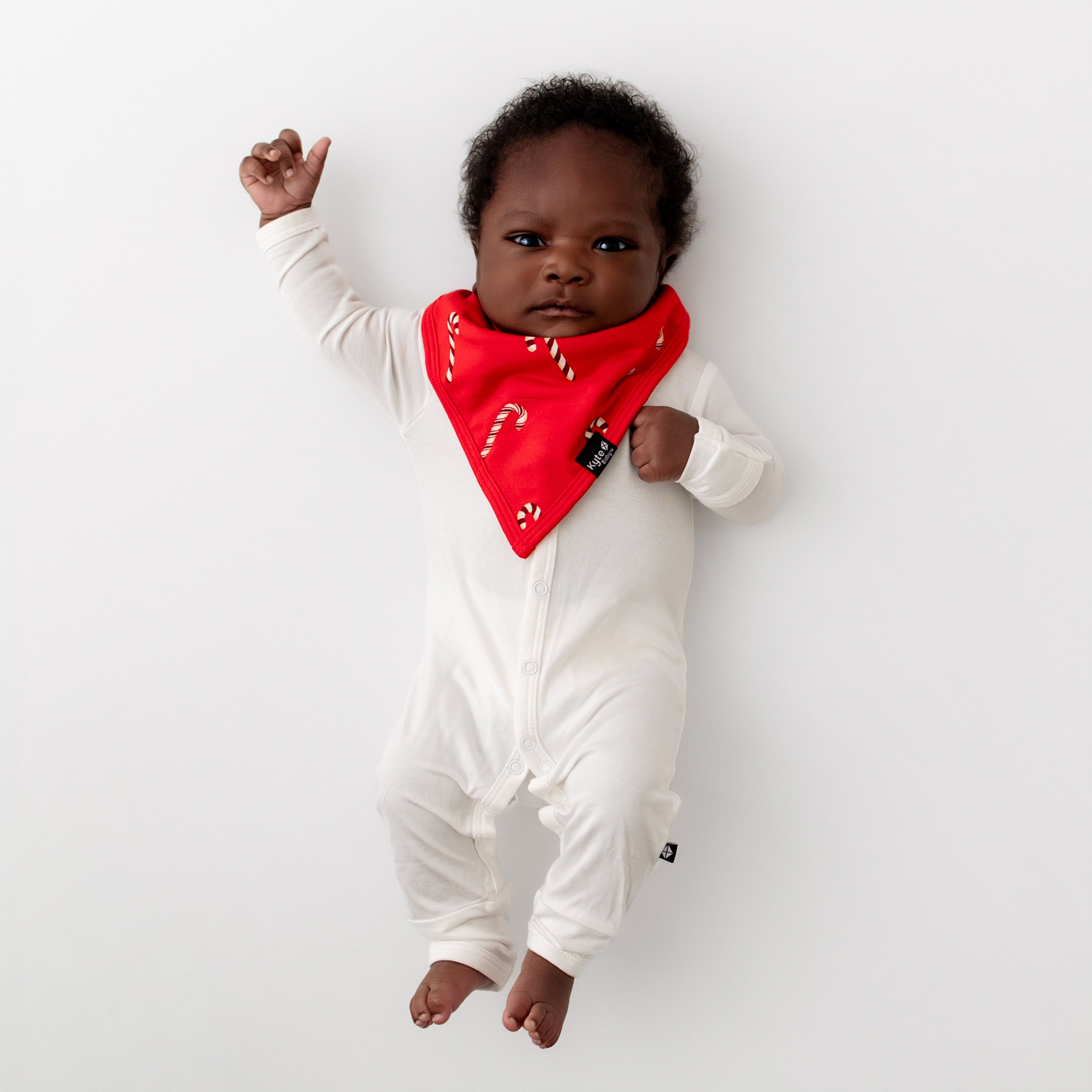Newborn baby laying down wearing the Bib in Candy Cane with a Cloud Snap Romper