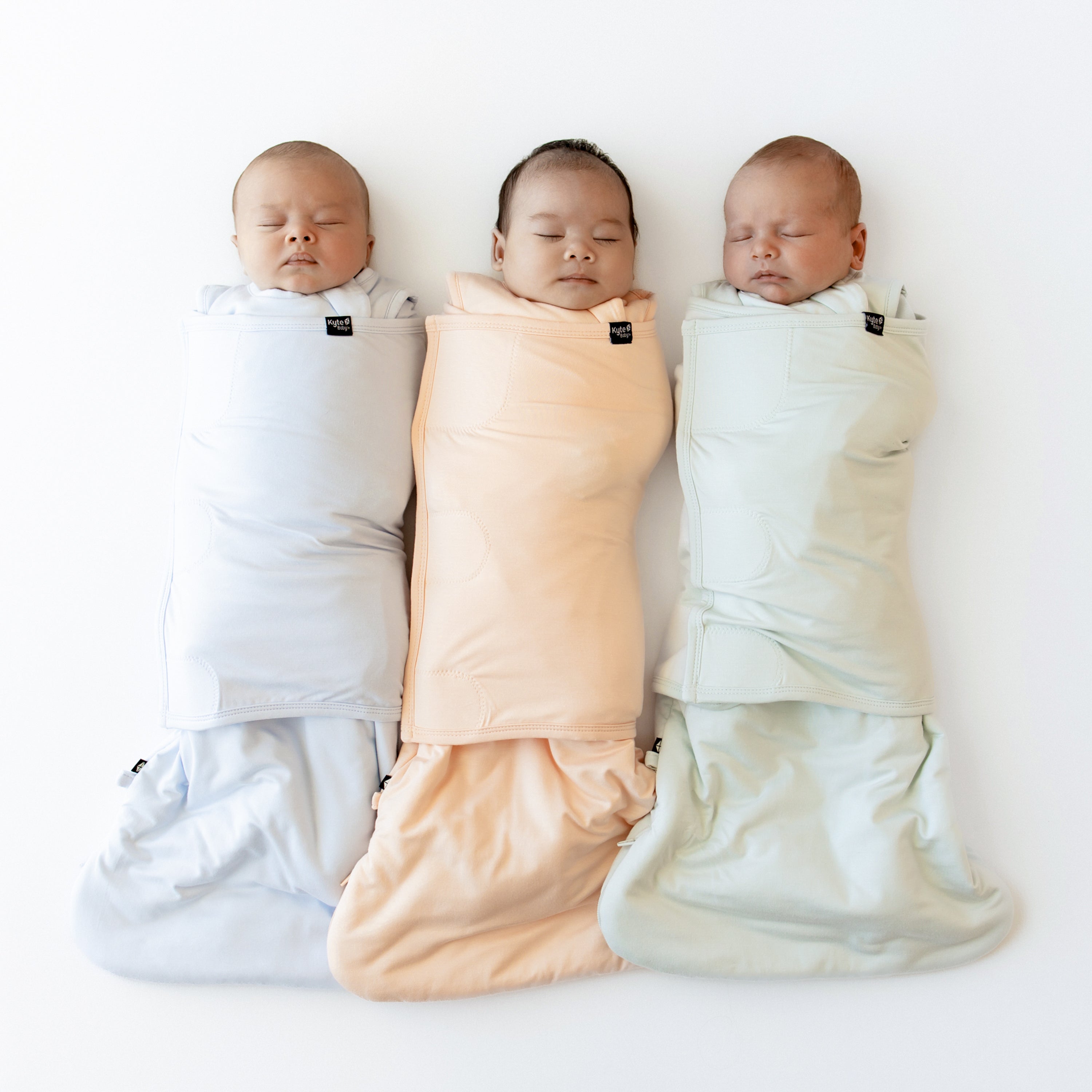 Three babies swaddled in Sleep Bag Swaddlers in Mist, Canyon and Dew