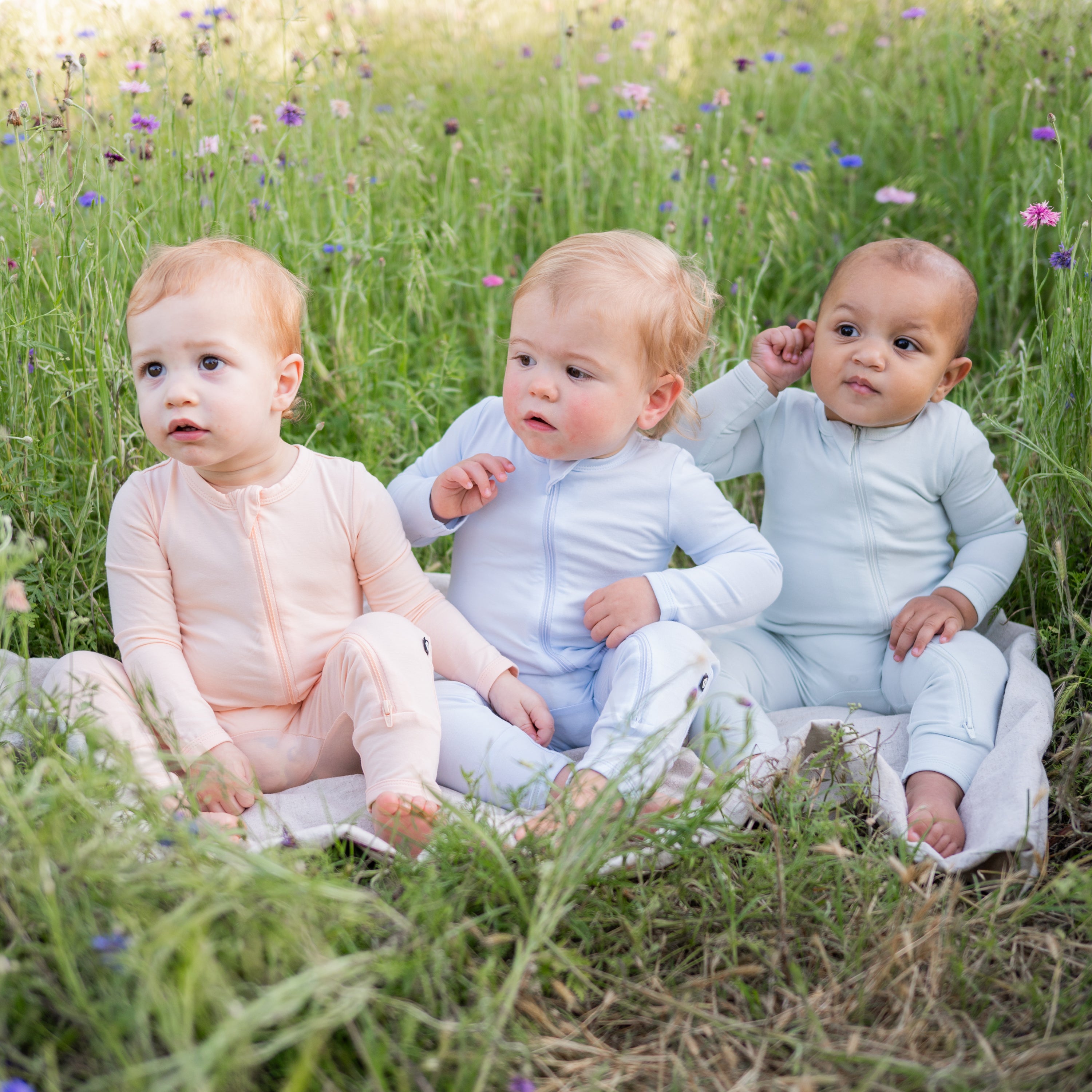 3 sitting babies in Kyte Baby Zippered Rompers in the colors Canyon, Mist and Dew