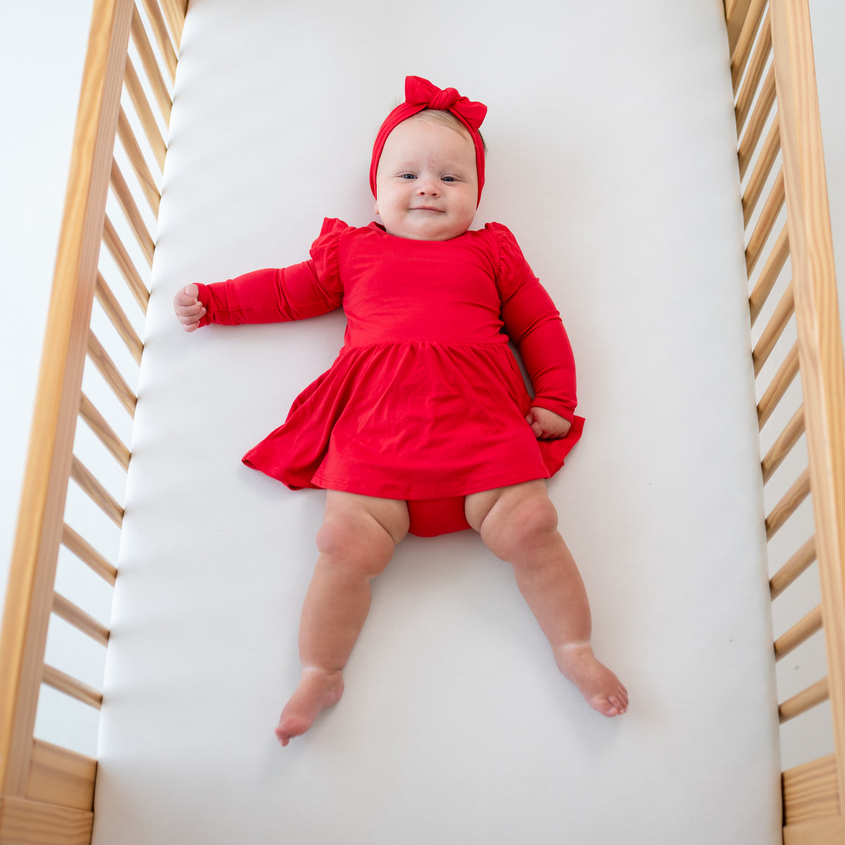Baby wearing Long Sleeve Twirl Bodysuit Dress in Cardinal and matching bow