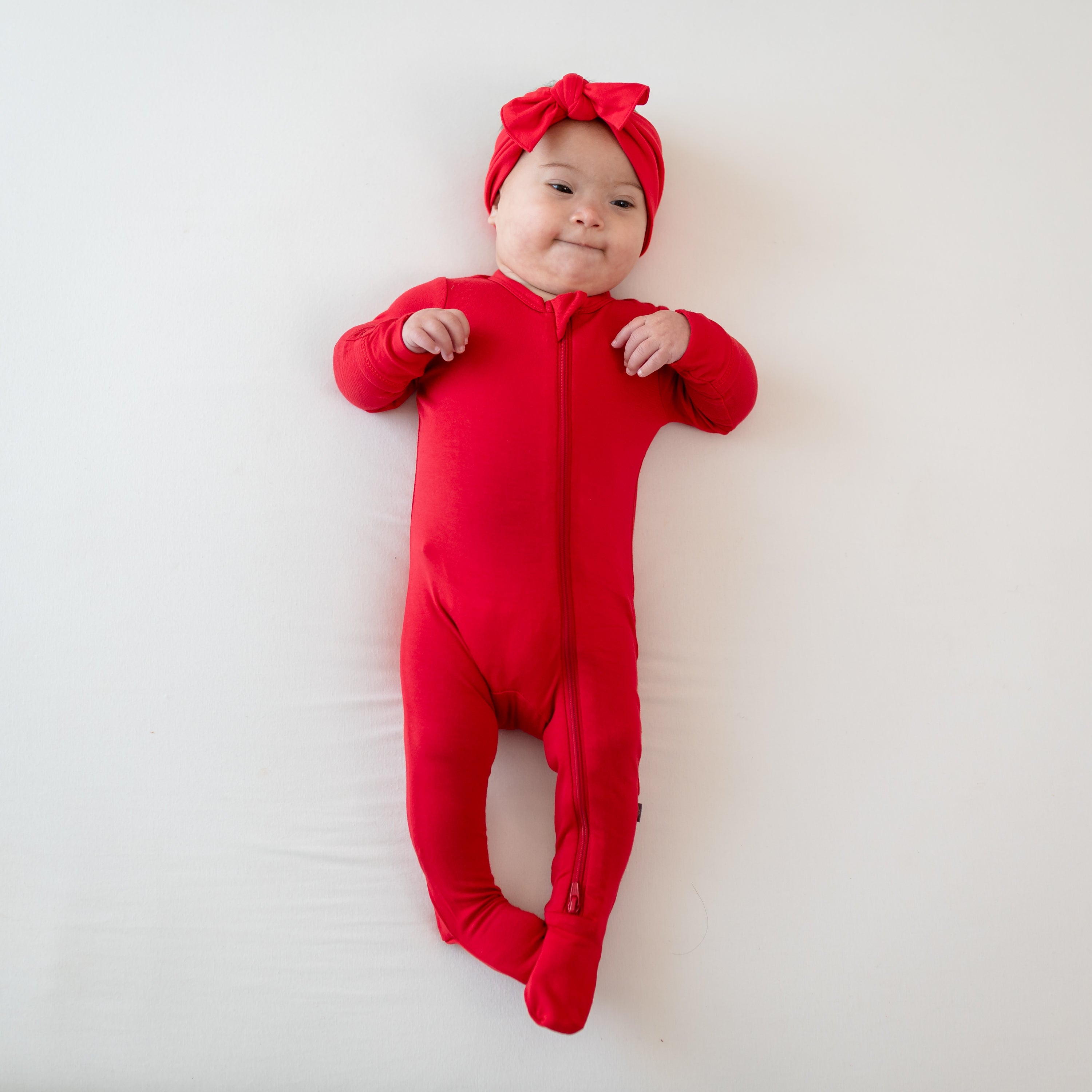 Baby modeling Zippered Footie in Cardinal and bow