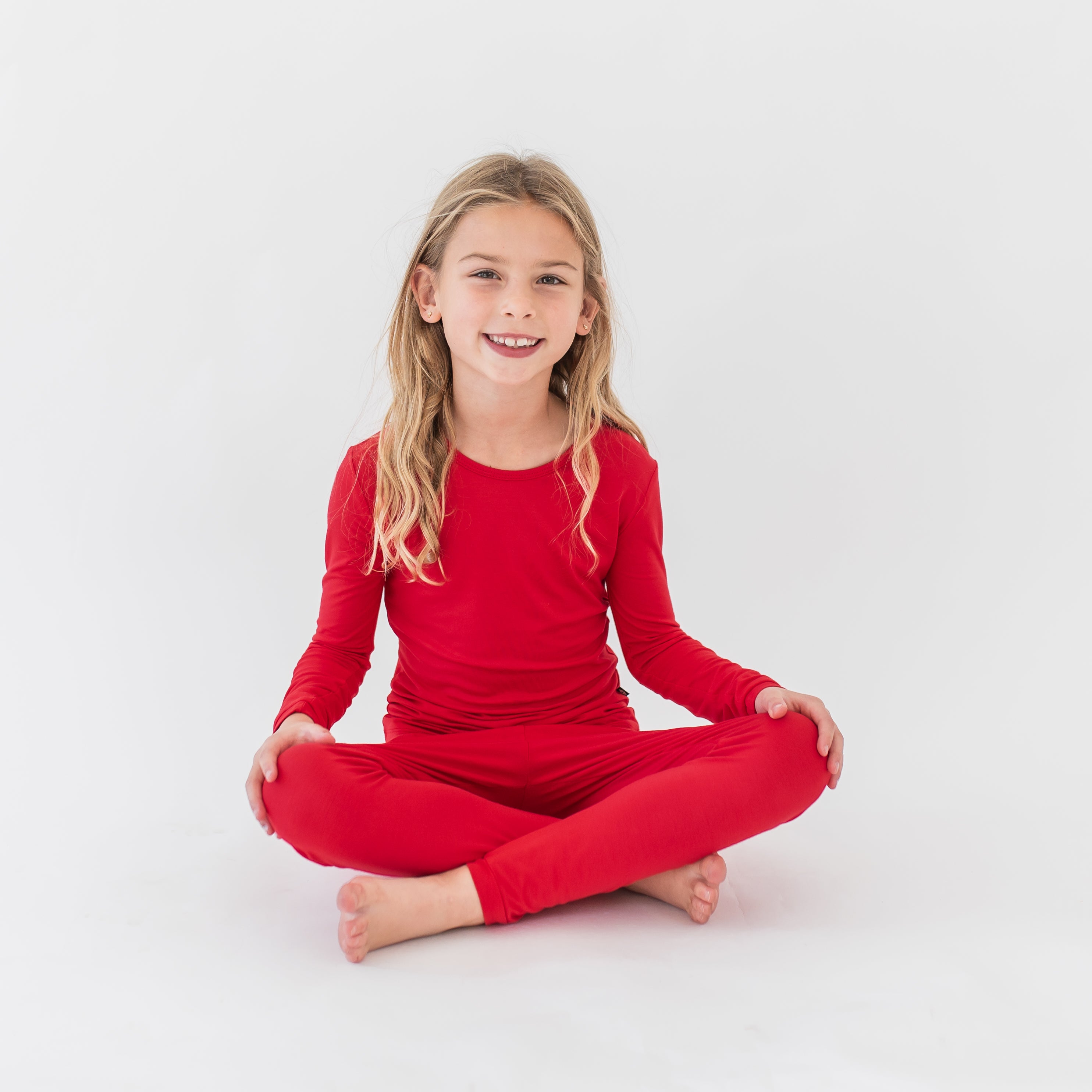 Young girl sitting cross legged on the floor wearing the Long Sleeve Pajamas in Cardinal