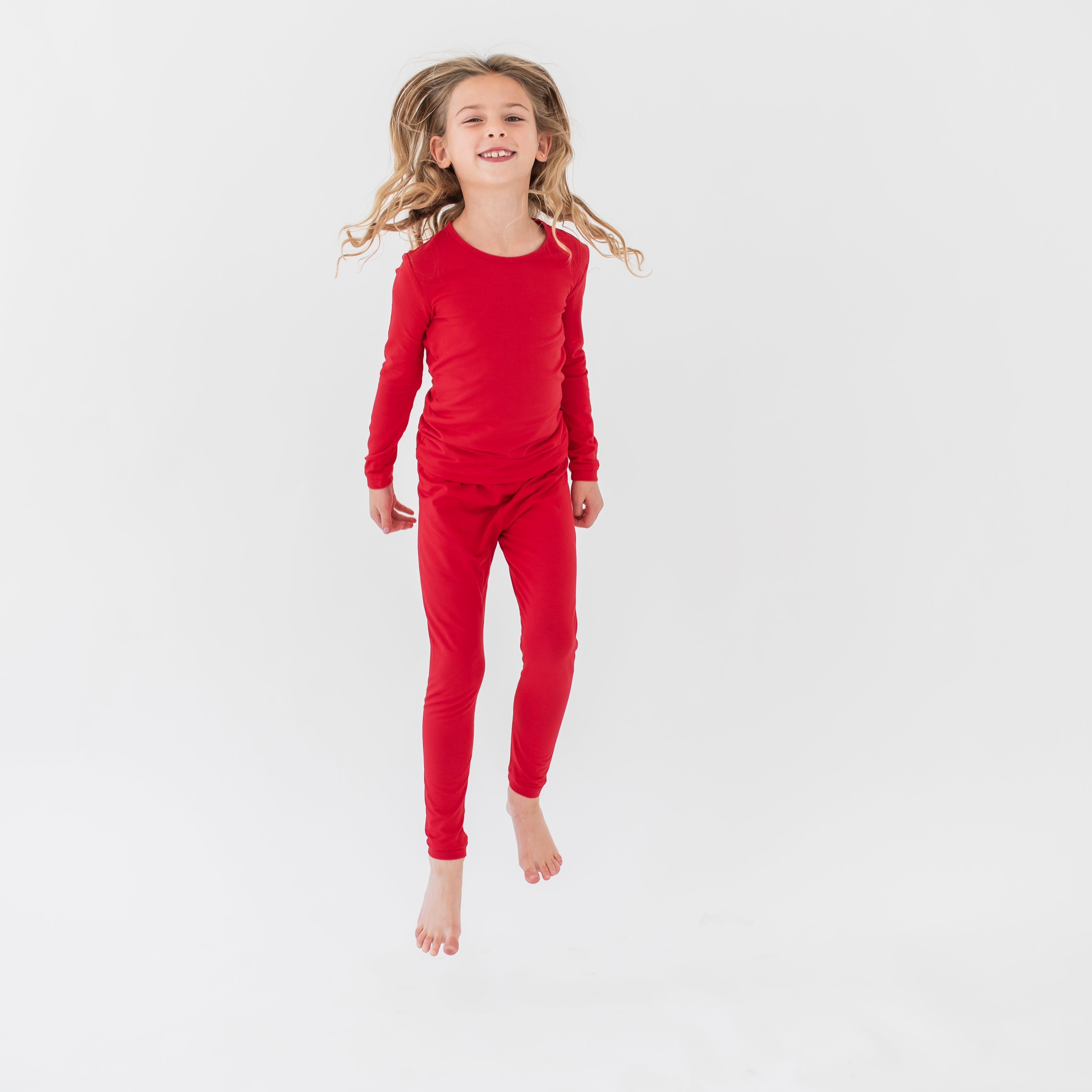 Young girl jumping wearing the Long Sleeve Pajamas in Cardinal in front of a white background