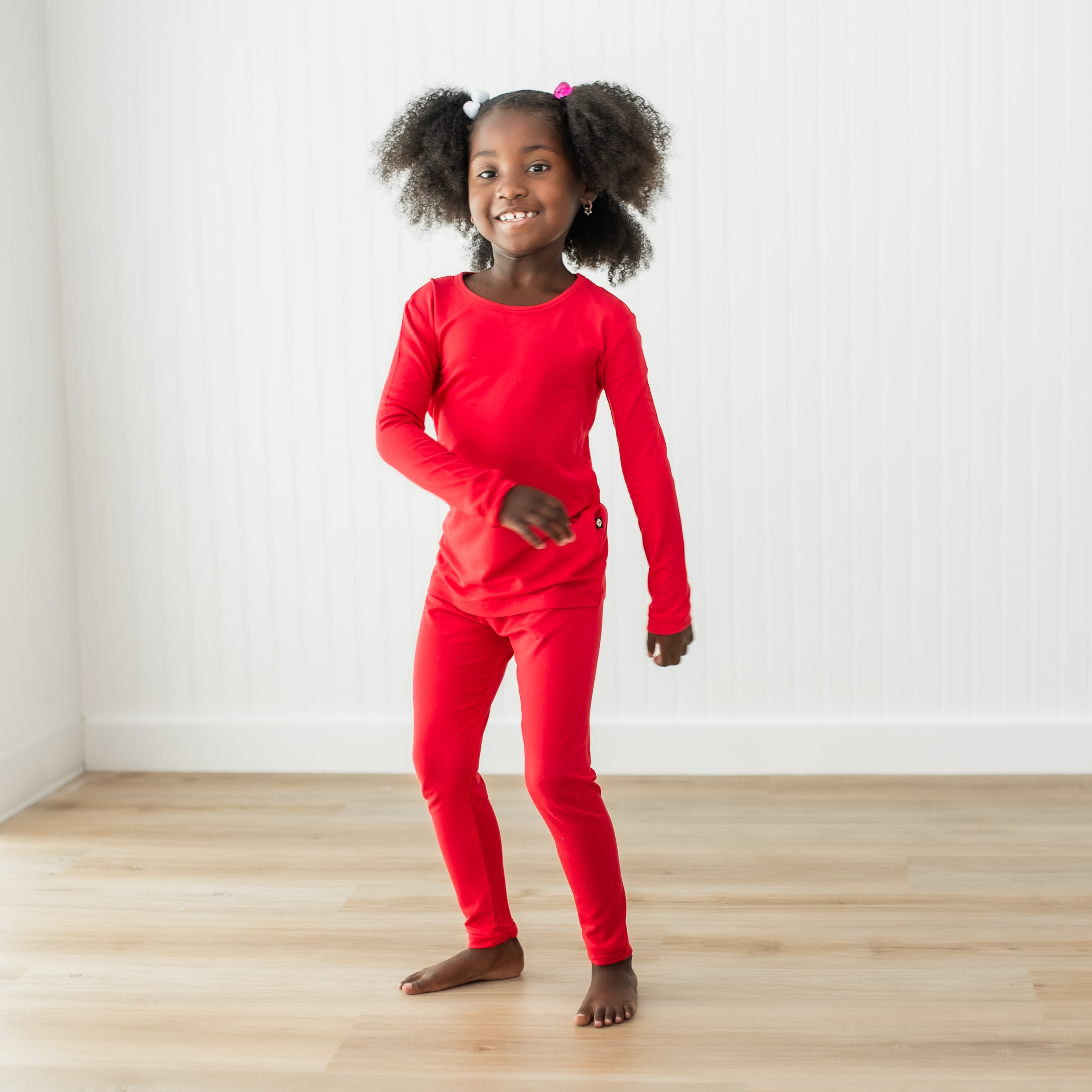 Young girl wearing a red pajama standing on a wooden floor with a white wall background