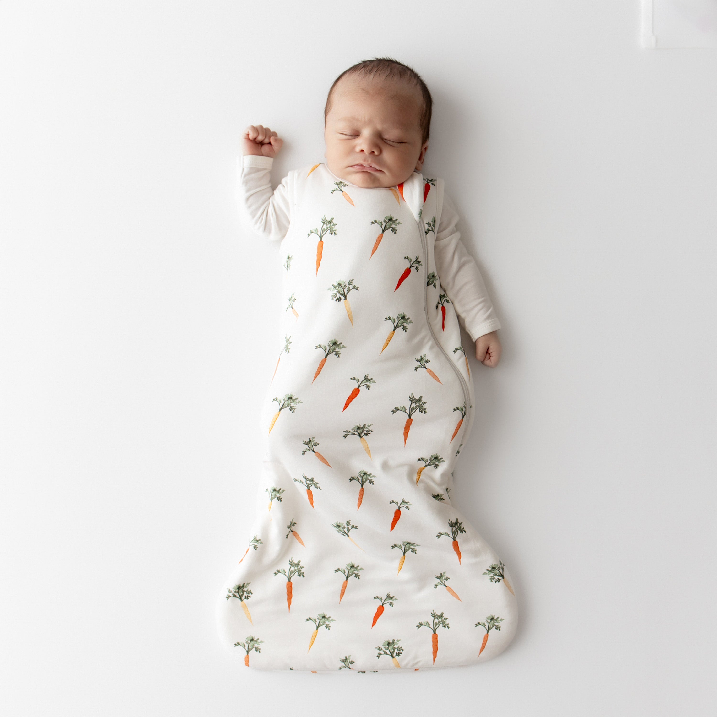 Sleeping newborn wearing the Sleep Bag in Carrot 1.0 with white long sleeve romper on underneath