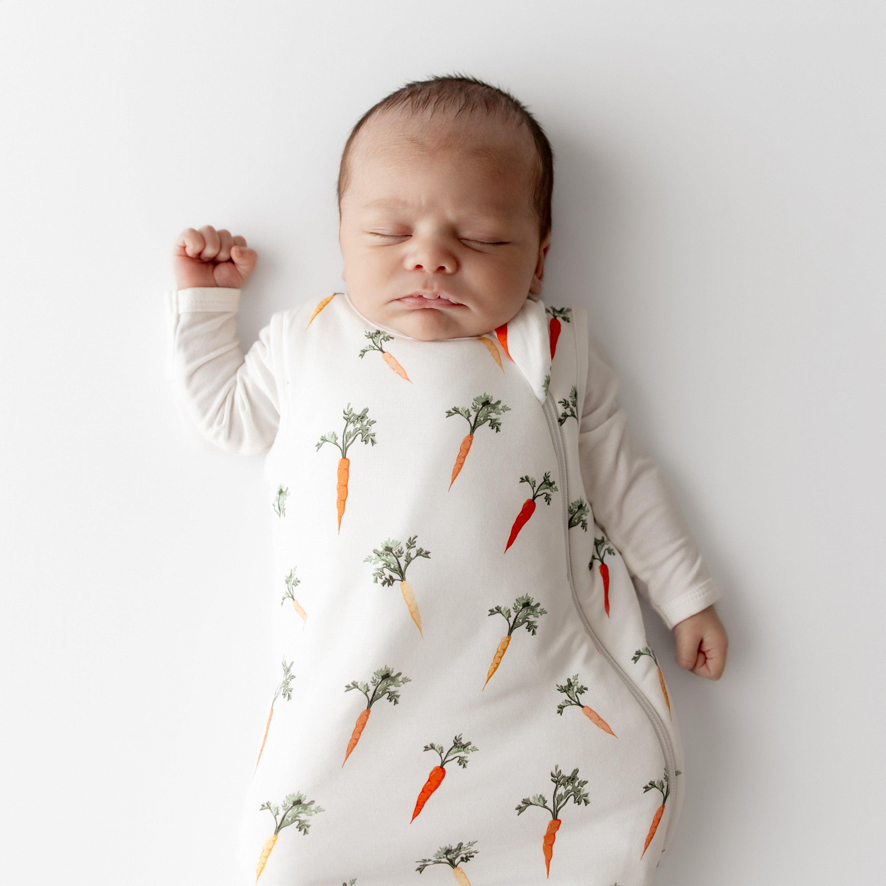 Close up of sleeping newborn wearing the Sleep Bag in Carrot 1.0 with white long sleeve romper on underneath