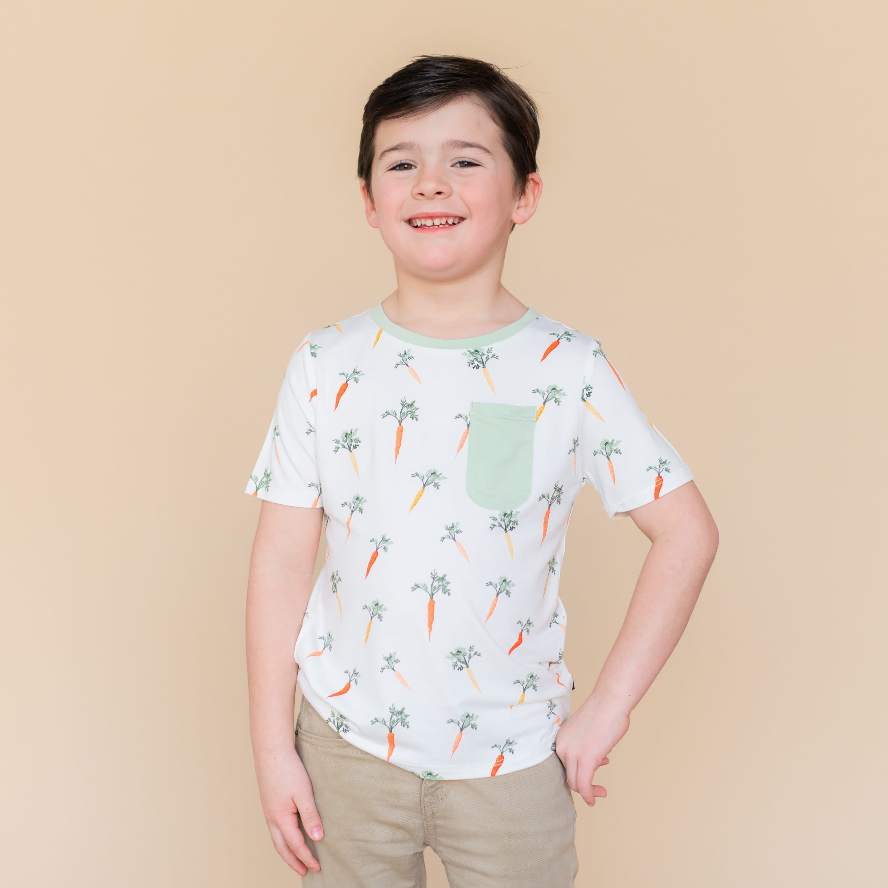 Smiling boy modeling the Toddler Crew Neck Tee in Carrot standing in front of a light neutral background