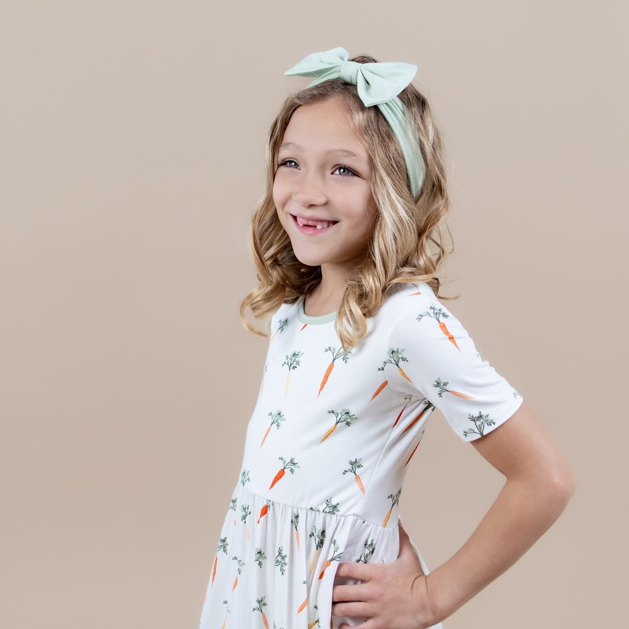 Smiling model posing wearing the Twirl Dress in Carrot paired with a light green bow